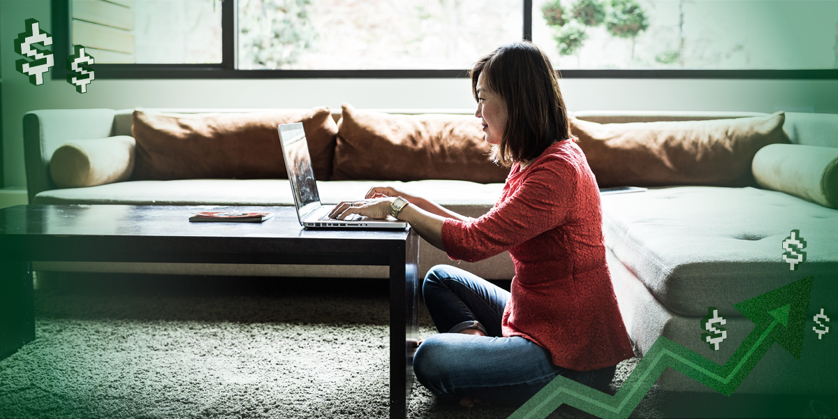 Asian woman sitting on the floor in front of her coffee table on a laptop at home.