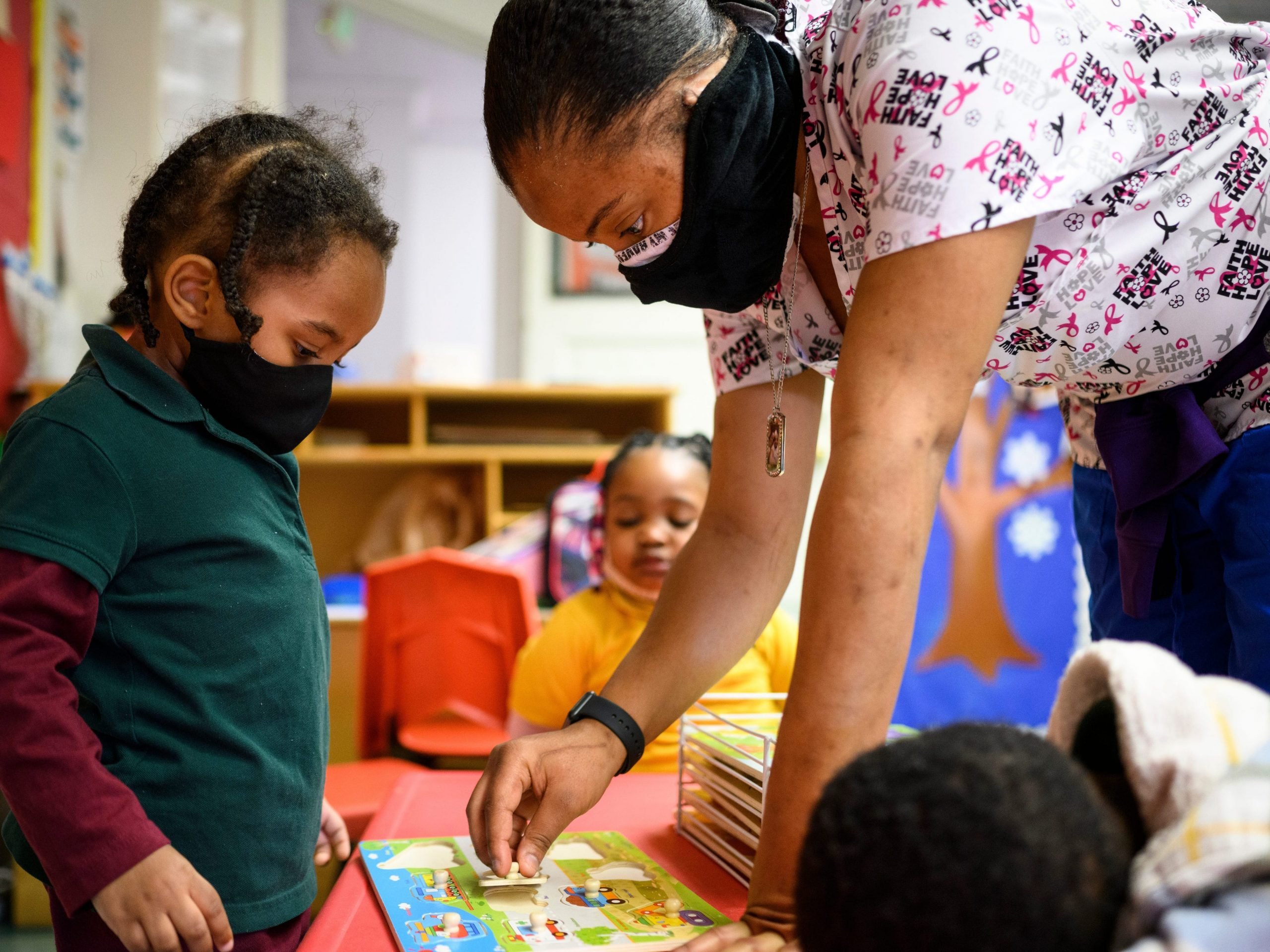 Shanikia Johnson, a three-year-olds teacher, helps Magjor Jones clean up a puzzle at Little Flowers Early Childhood and Development Center in the Sandtown-Winchester neighborhood of Baltimore, Maryland on January 12, 2021