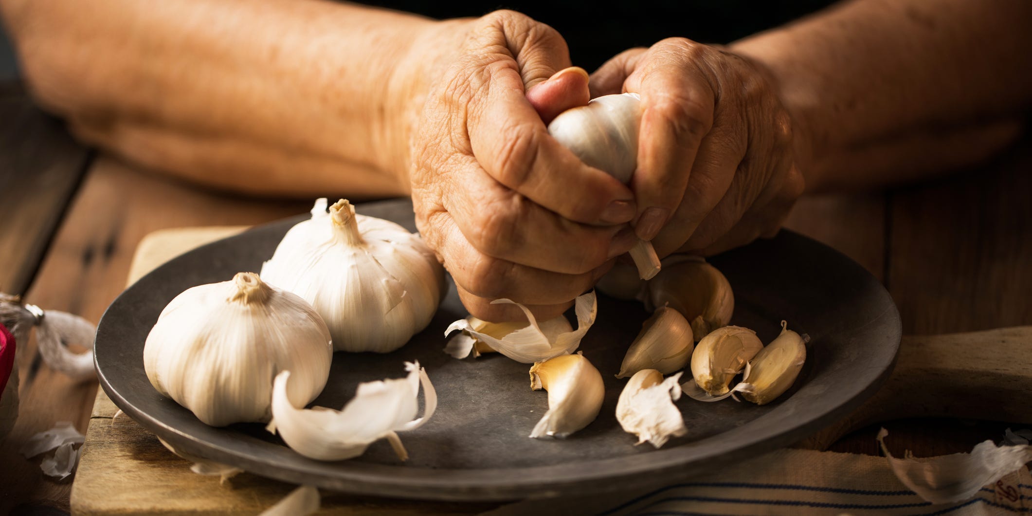 A closeup of an older woman's hands separating garlic bulbs into cloves