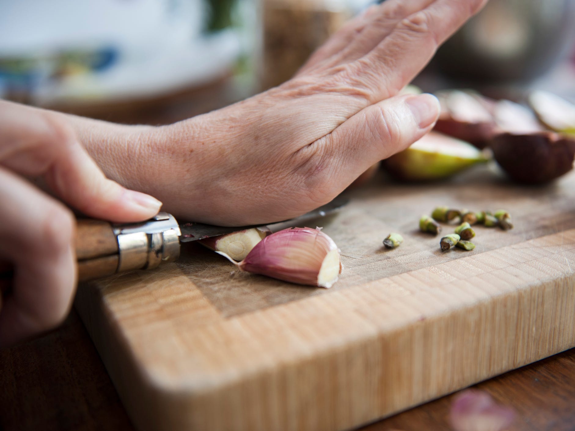 A closeup of a person's hands using the flat part of the knife blade to crush a clove of garlic