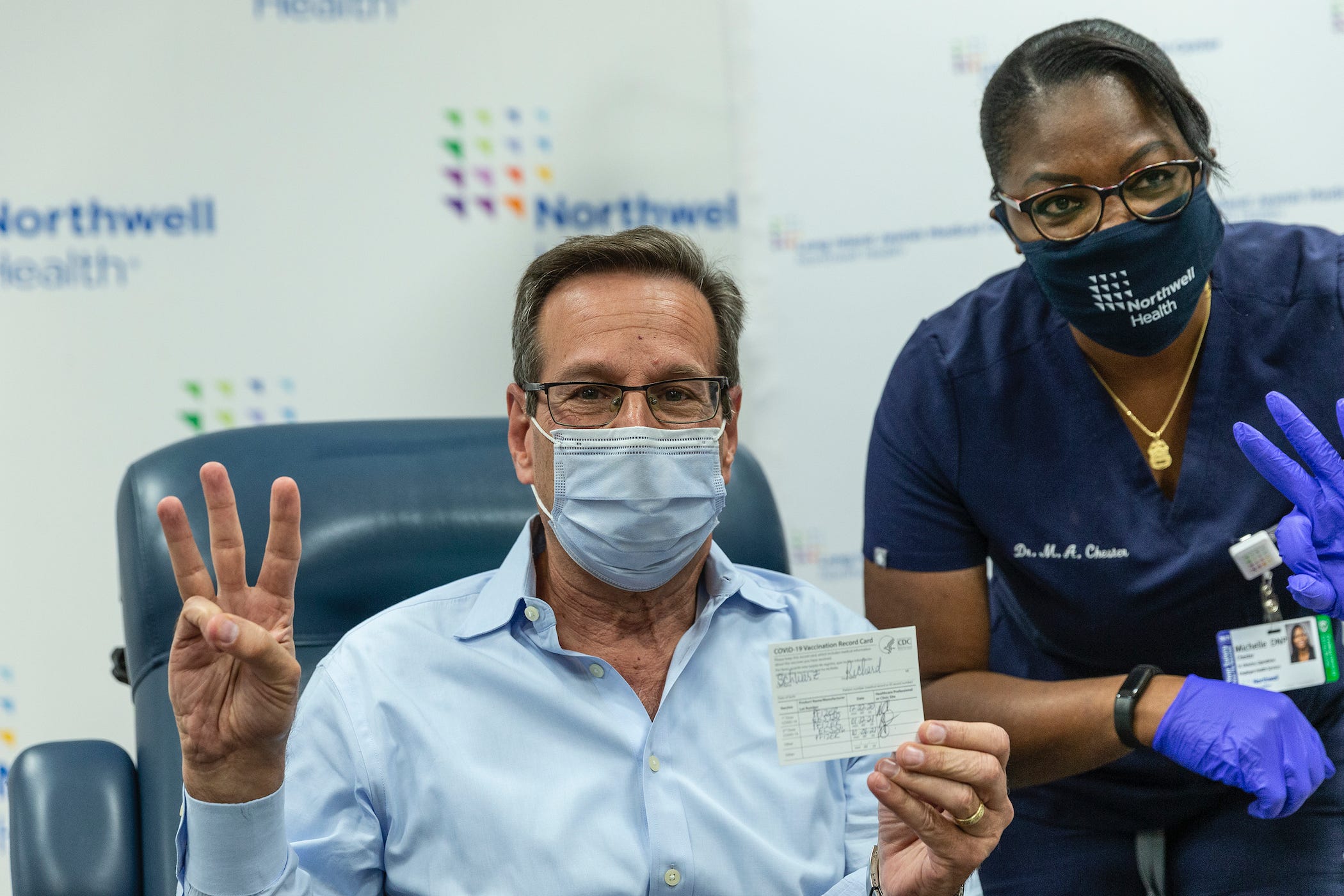 a man holds up three fingers, and his filled out CDC vaccine card, after getting a booster shot.