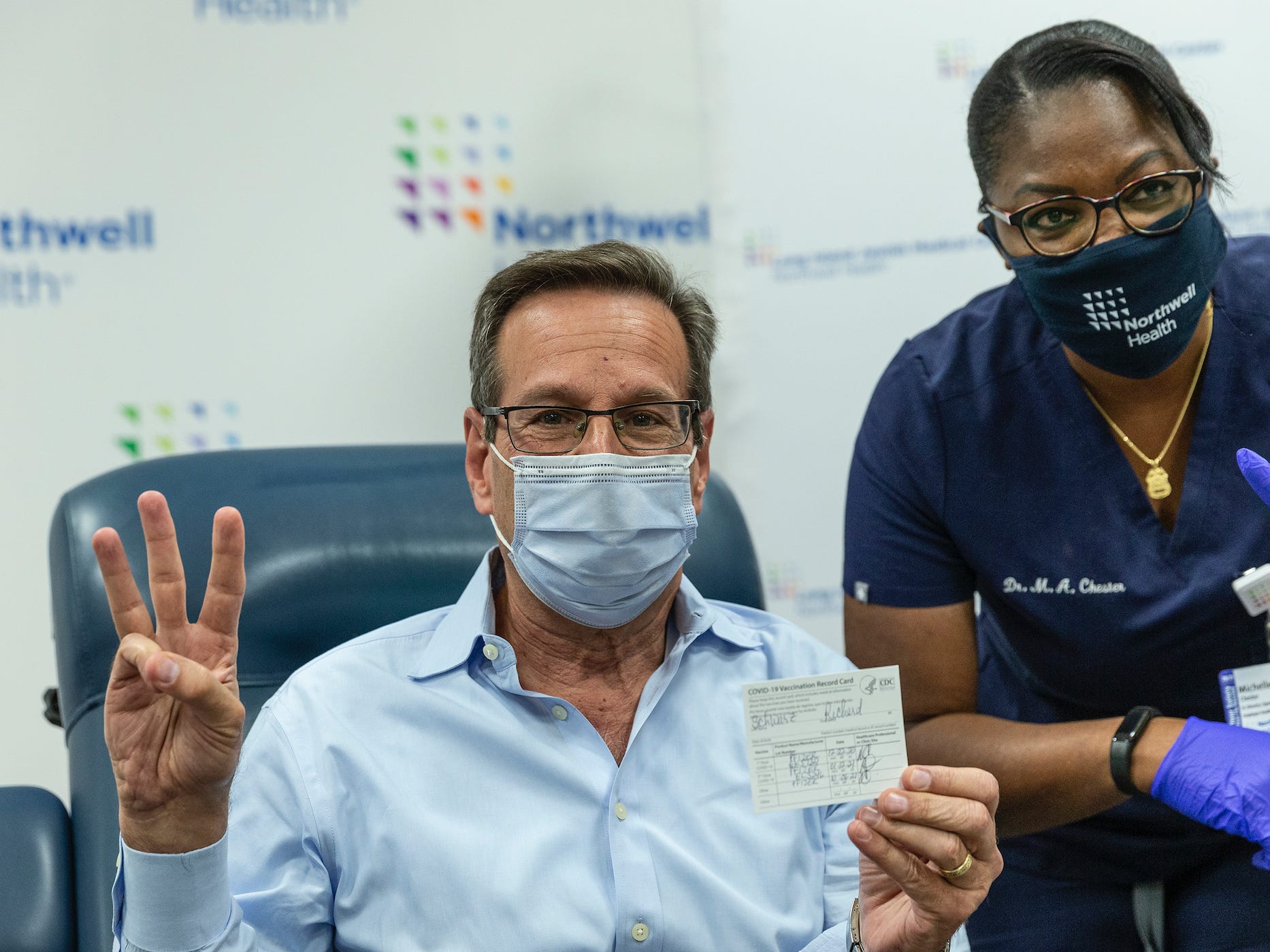 a man holds up three fingers, and his filled out CDC vaccine card, after getting a booster shot.