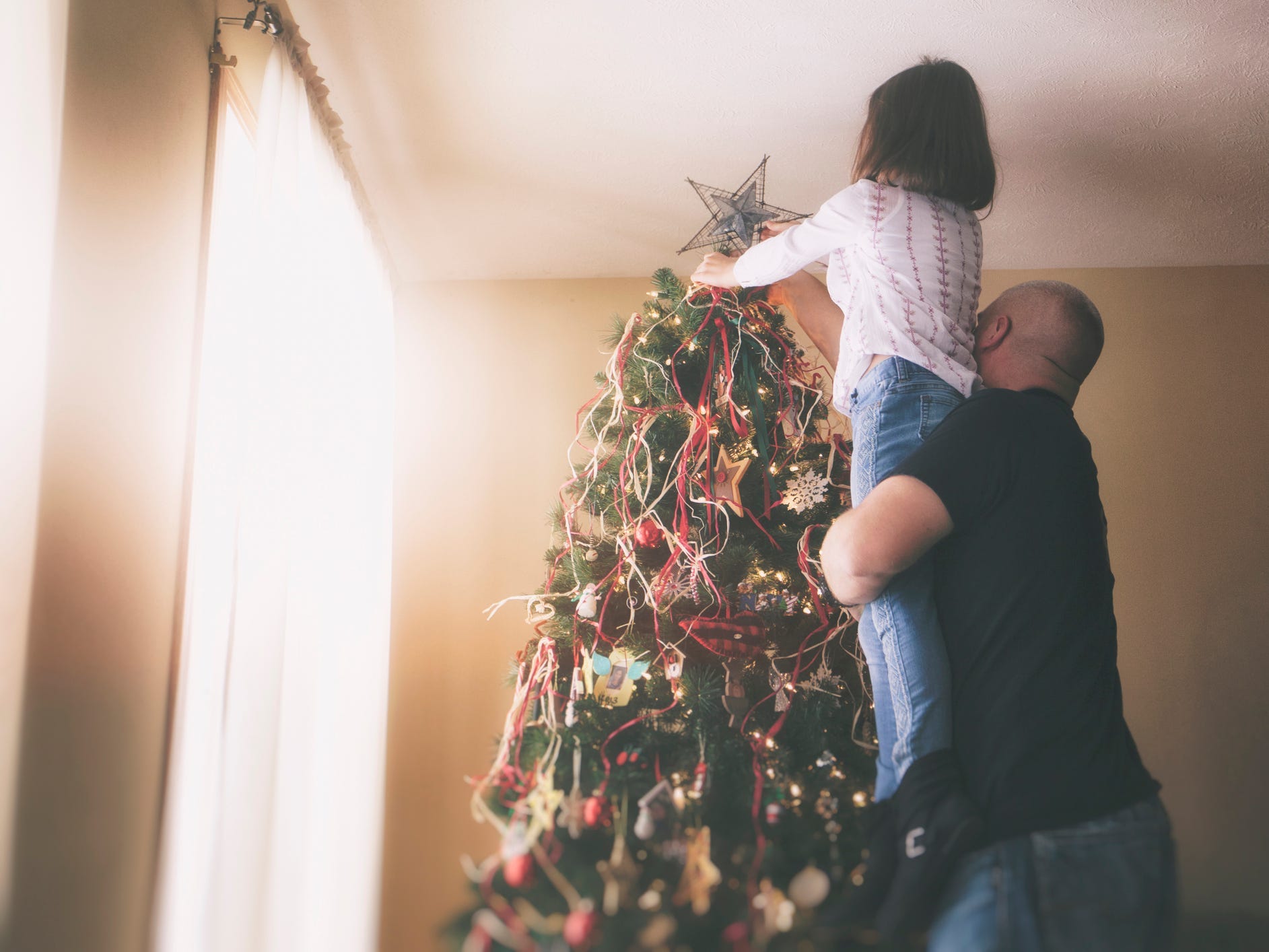 A parent helping their child put a star on top of a tree.