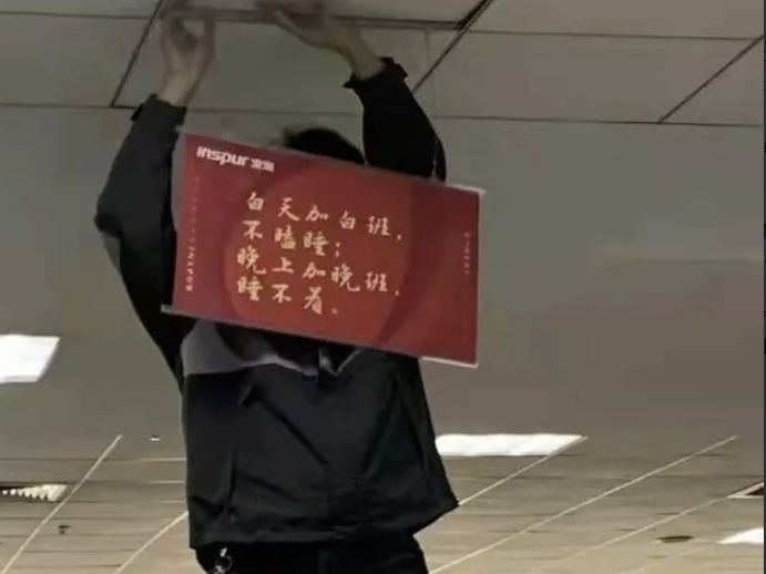 Man putting up a banner in Chinese extolling overtime work.