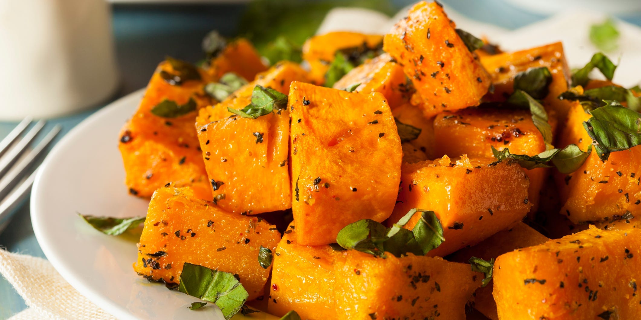 A plate of roasted butternut squash cubes topped with pepper and herbs