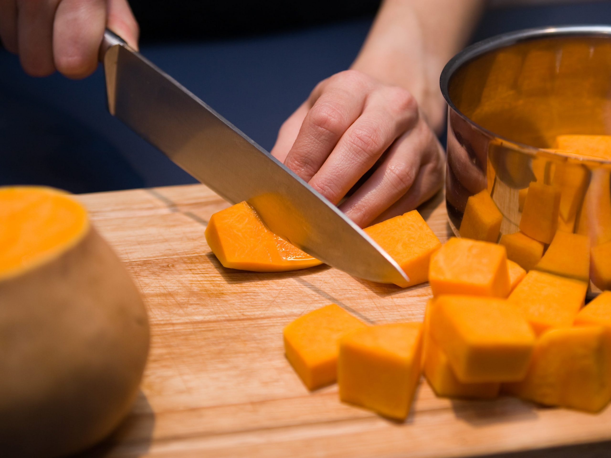 A closeup of a person's hands cutting butternut squash into cubes