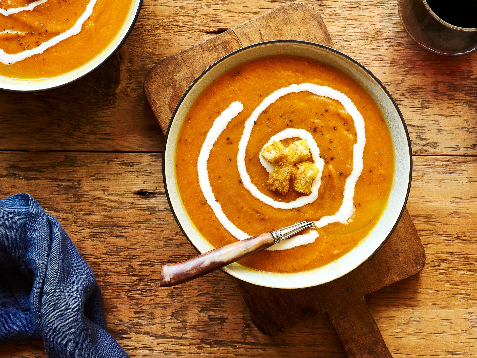 A top-down view of a bowl of butternut squash soup topped with a swirl of cream and croutons