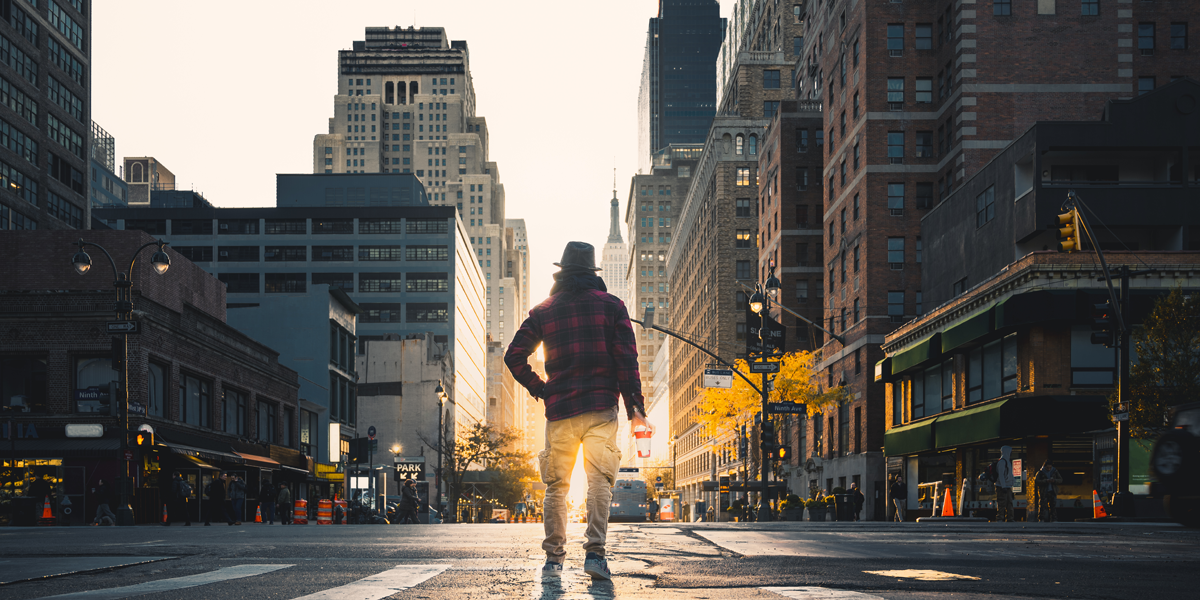 Man holding a paper coffee cup standing in the middle of a street in NYC.