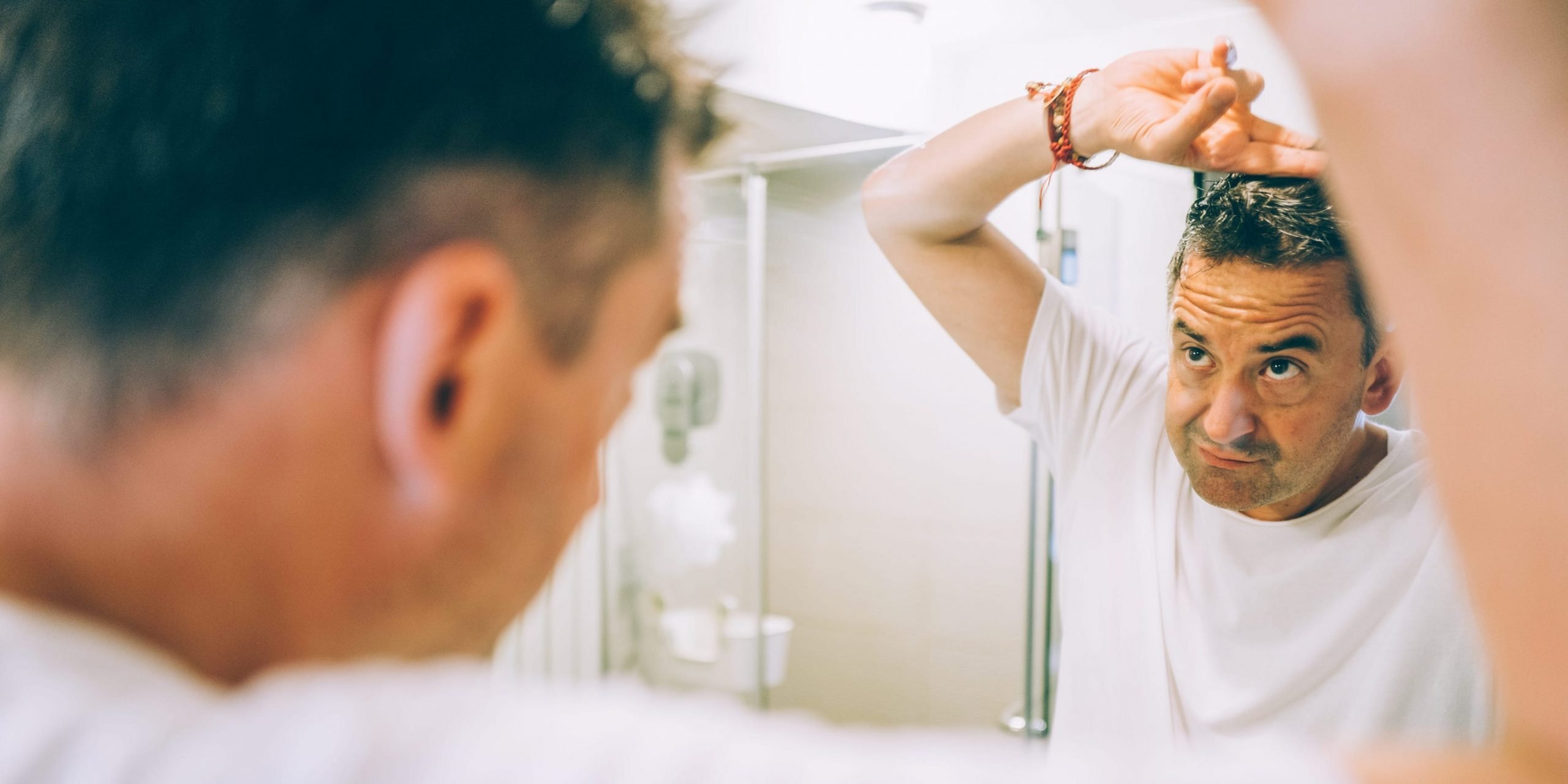 A middle-aged man checks his hair in a mirror.