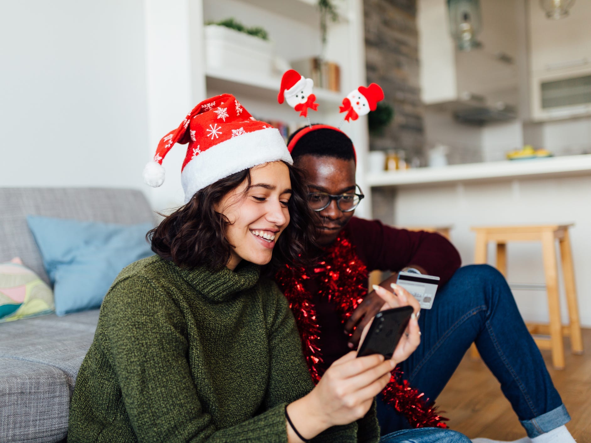 couple sitting on the floor in their home wearing holiday headbands shopping online from a smartphone