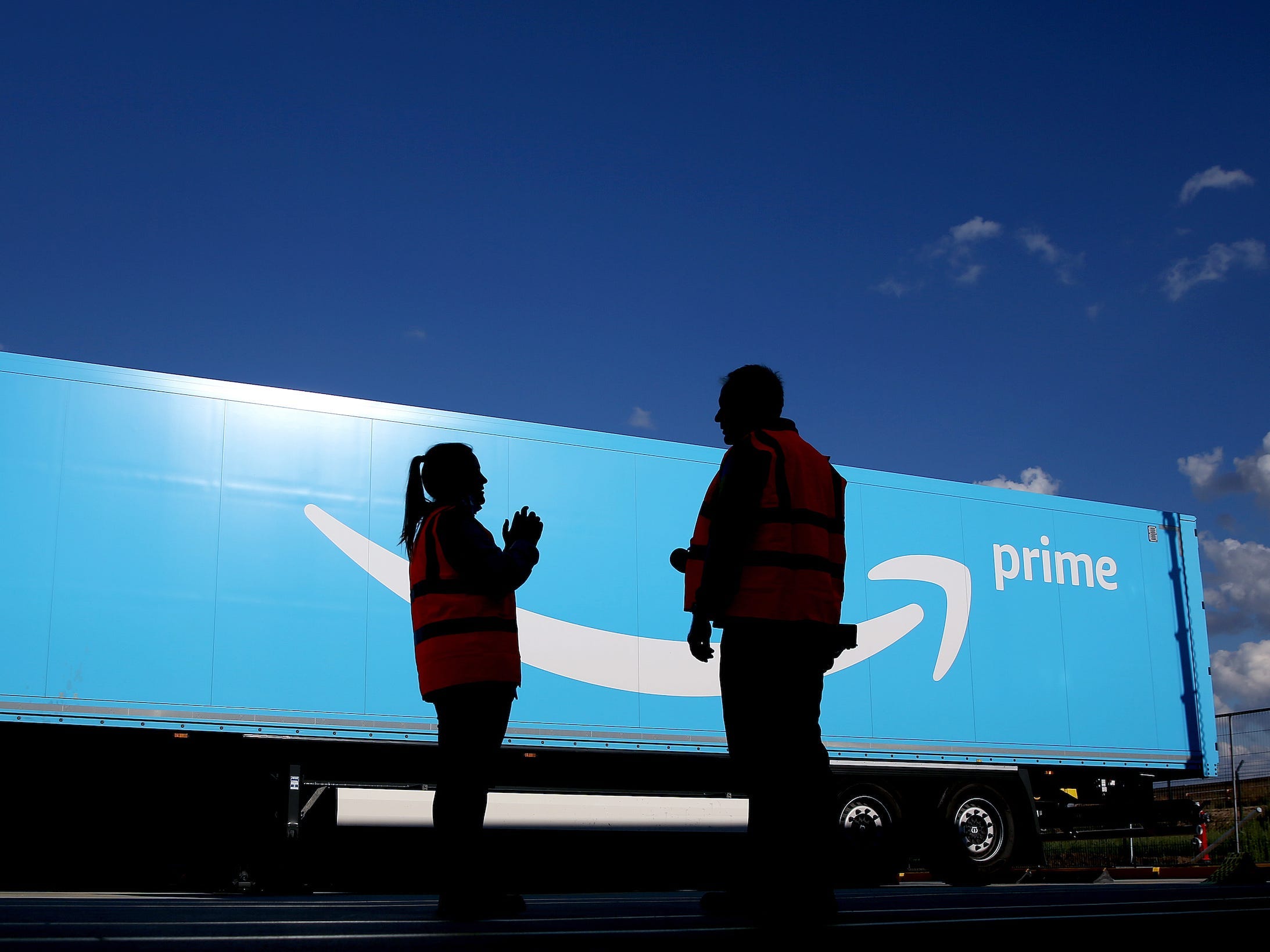 Amazon workers stand in front of a large "Amazon Prime" branded truck trailer.
