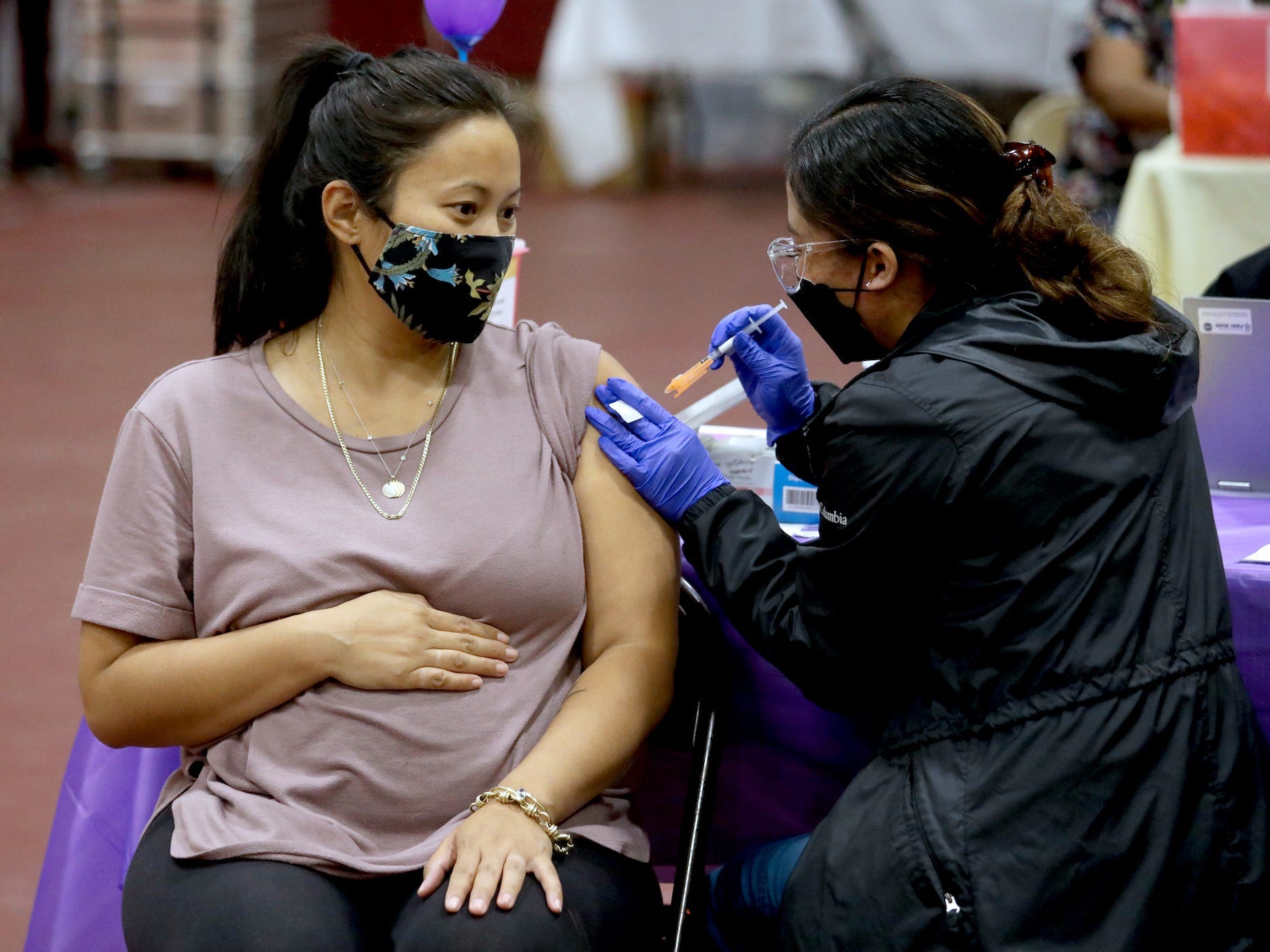 a pregnant woman, sitting and clutching her belly, getting a covid 19 booster shot stuck into her arm.