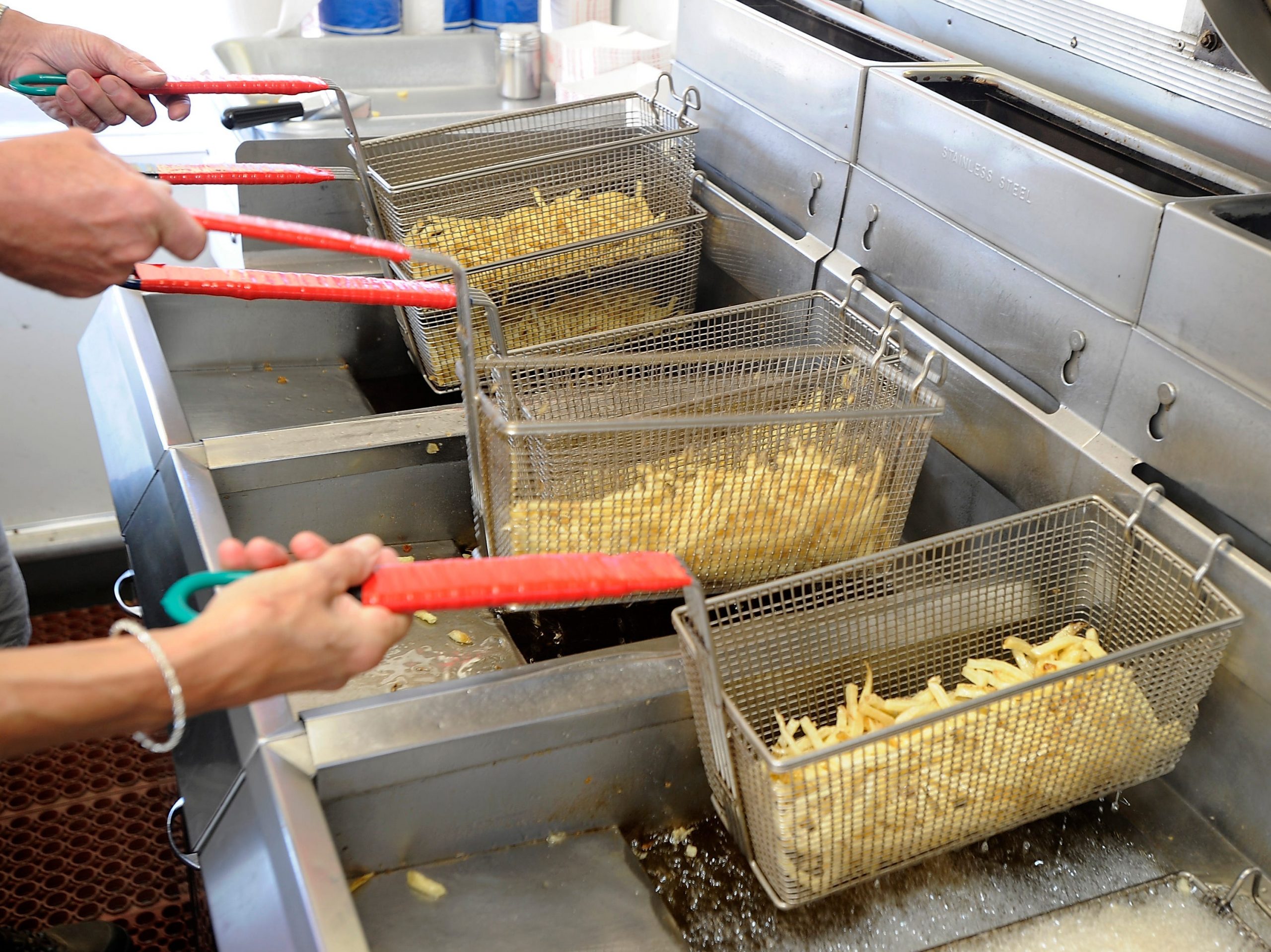 People lift french fries in baskets out of deep fryer filled with oil