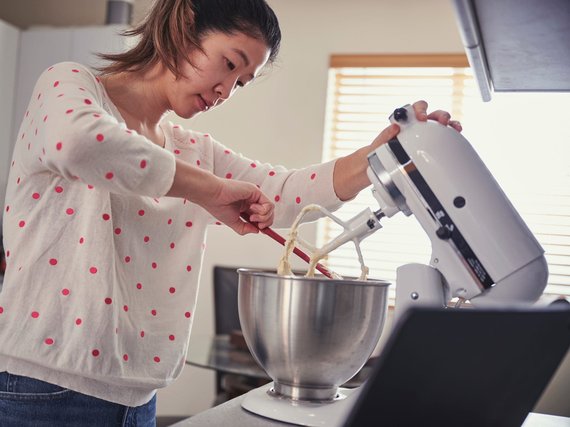 Woman scraping stuff off of a stand mixer.