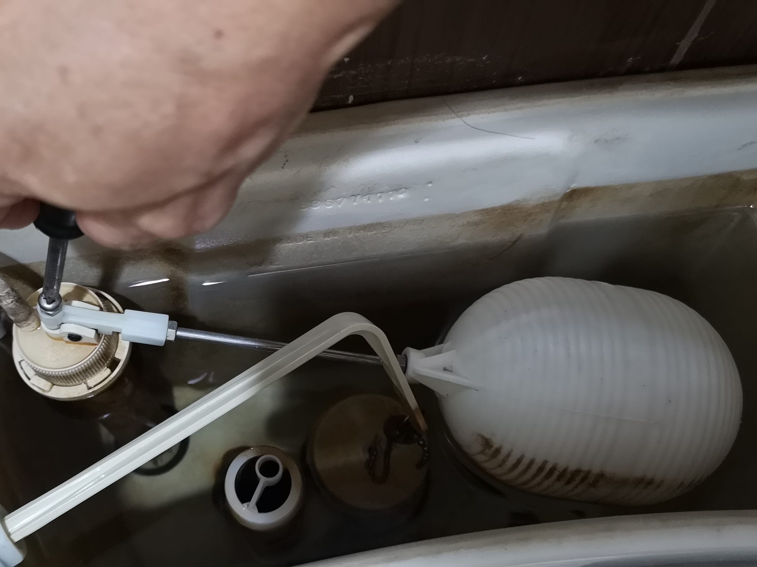A person's hand adjusting the float in a toilet tank