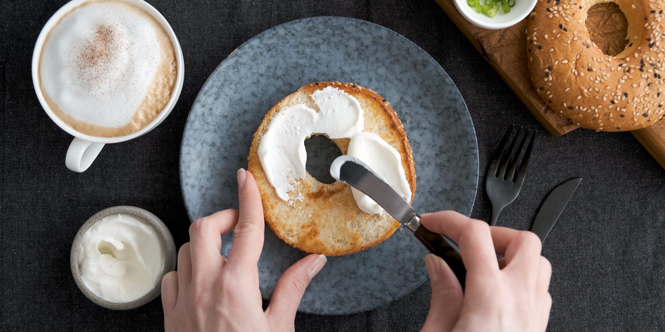 A top-down view of a pair of hands spreading cream cheese onto a toasted bagel