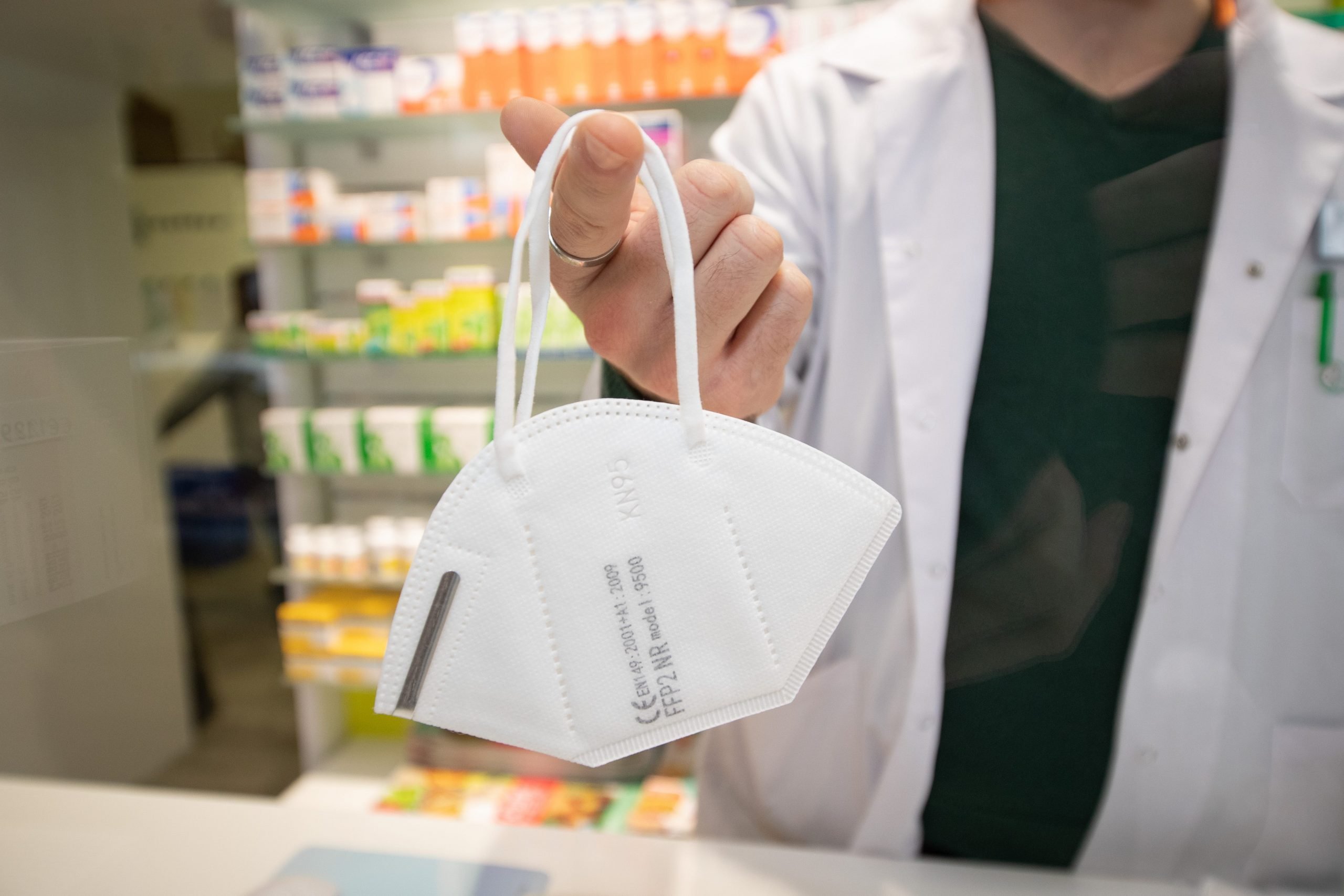 A pharmacist holds a mouth and nose protection mask on a finger.