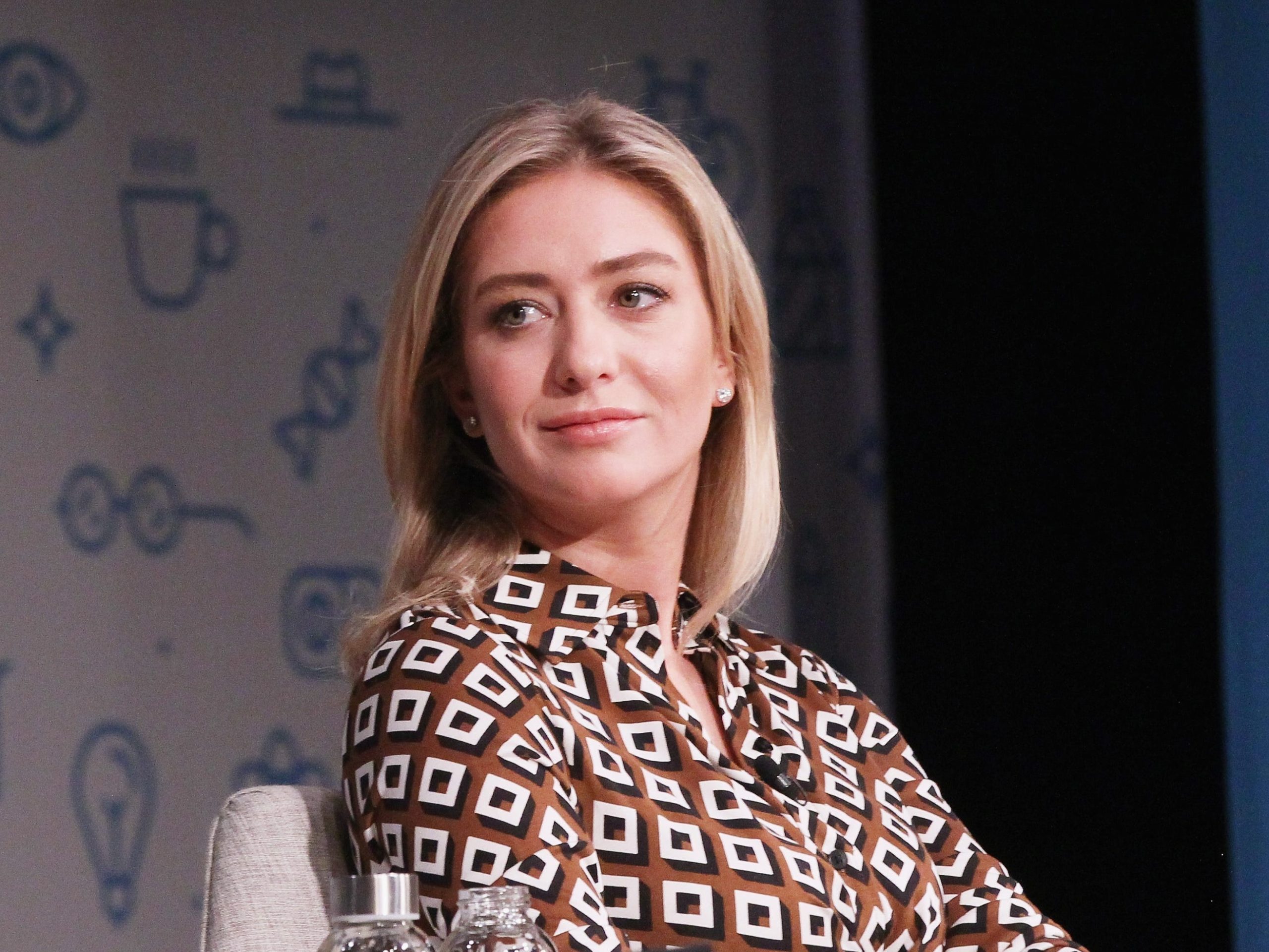 Whitney Wolfe Herd wears a brown and white dress while sitting on stage.