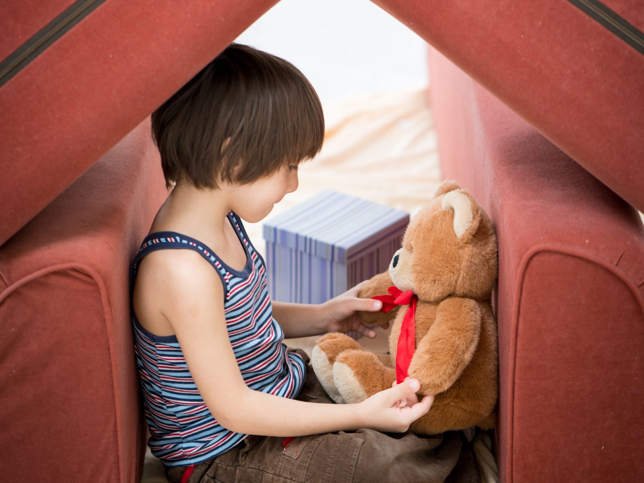Little boy and Teddy bear with small house made of furniture
