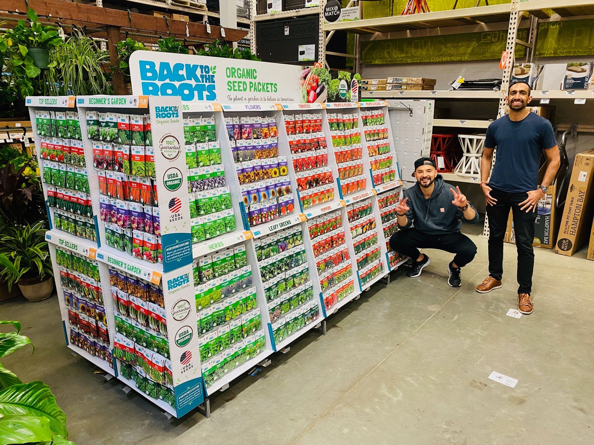 Back to the Roots co-CEOS Nikhil Arora (right) and Alejandro Velez stand next to a large seed display in a retail store.