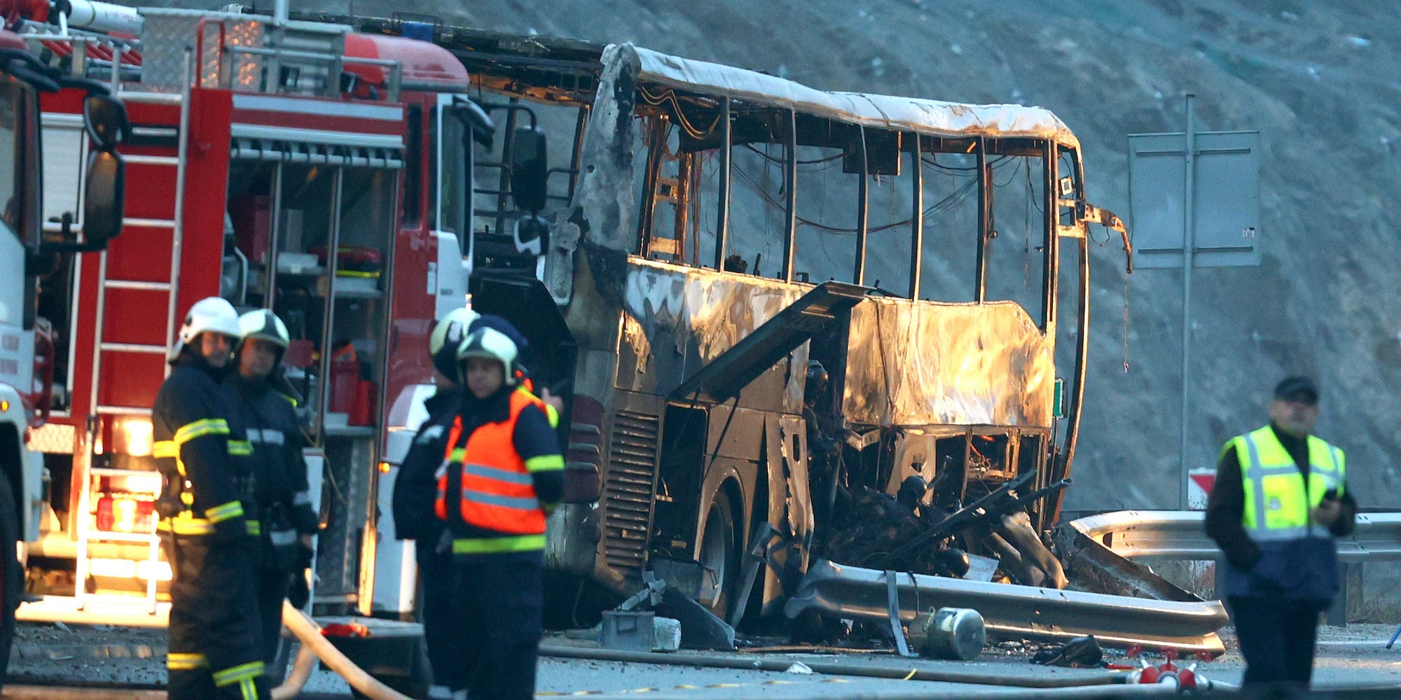 Firefighters stand beside a burnt-out bus