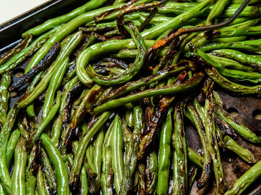 Roasted char-grilled green beans cooling in oven pan.