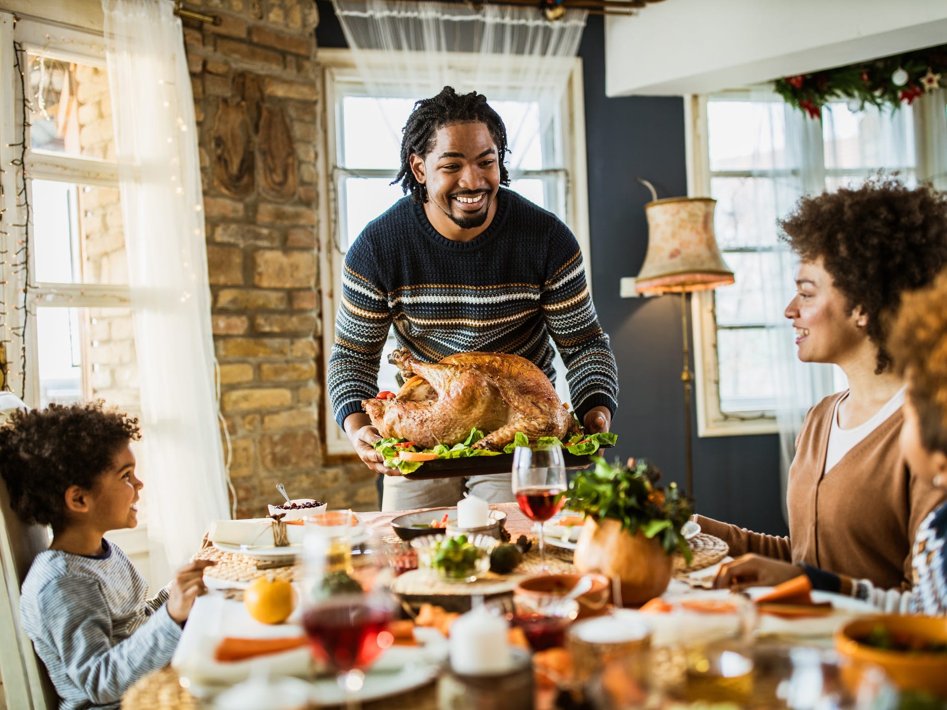 A man bringing a Thanksgiving turkey to the dinner table as his family watches