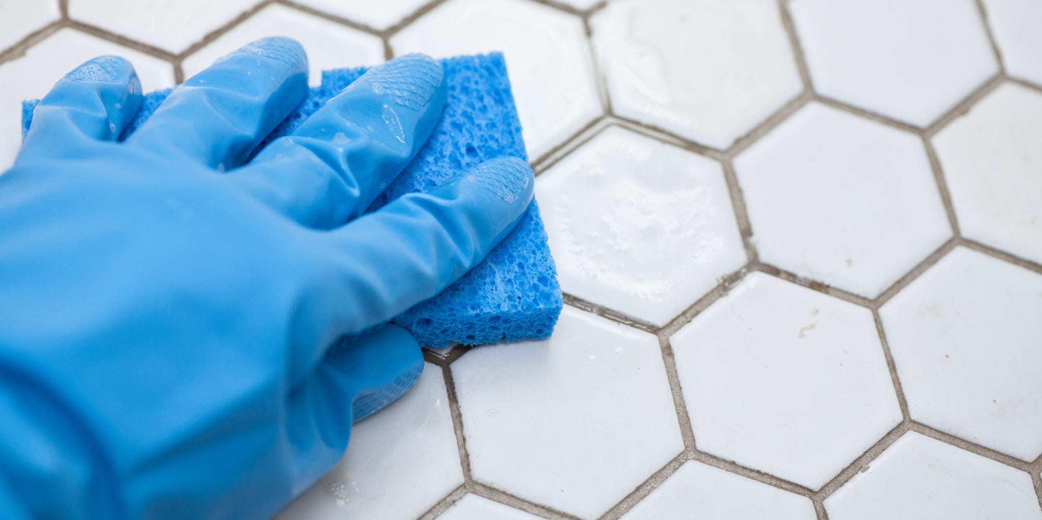 A gloved hand cleaning tile with a sponge