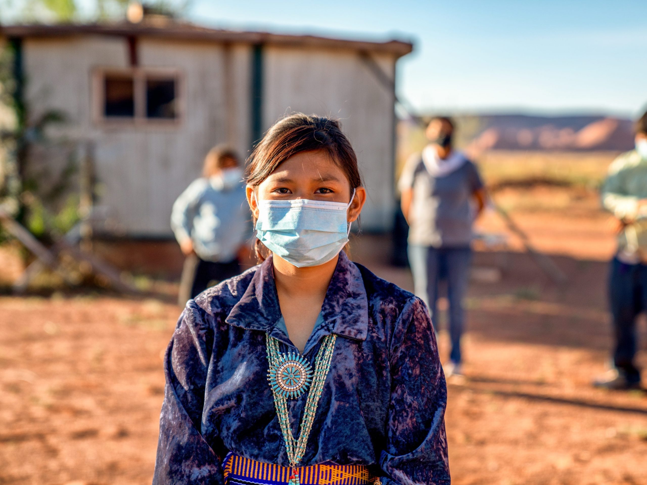 A Native woman wearing a mask with several men behind her out of focus