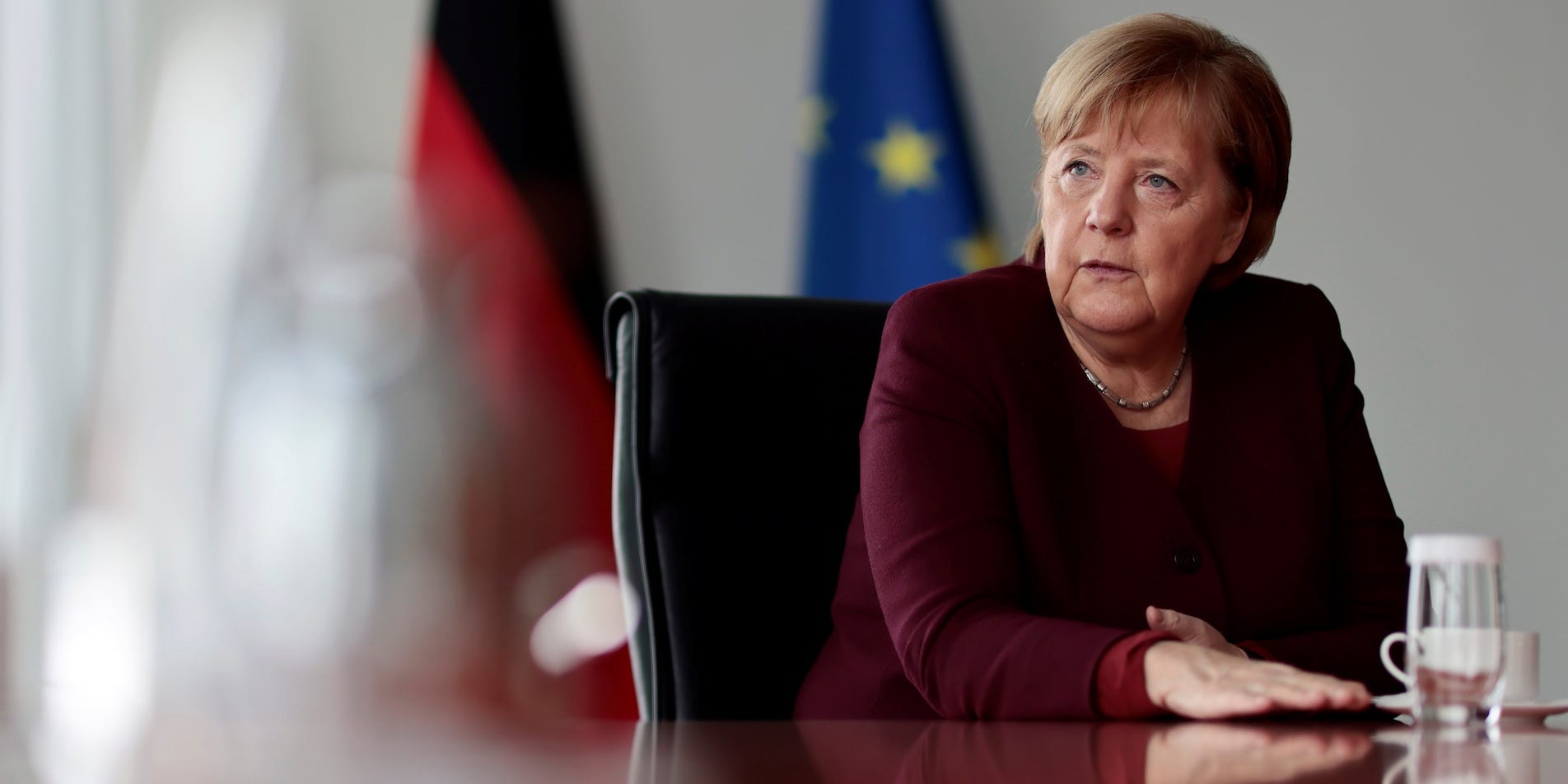 Angela Merkel seated at a table, with German and EU flags behind her