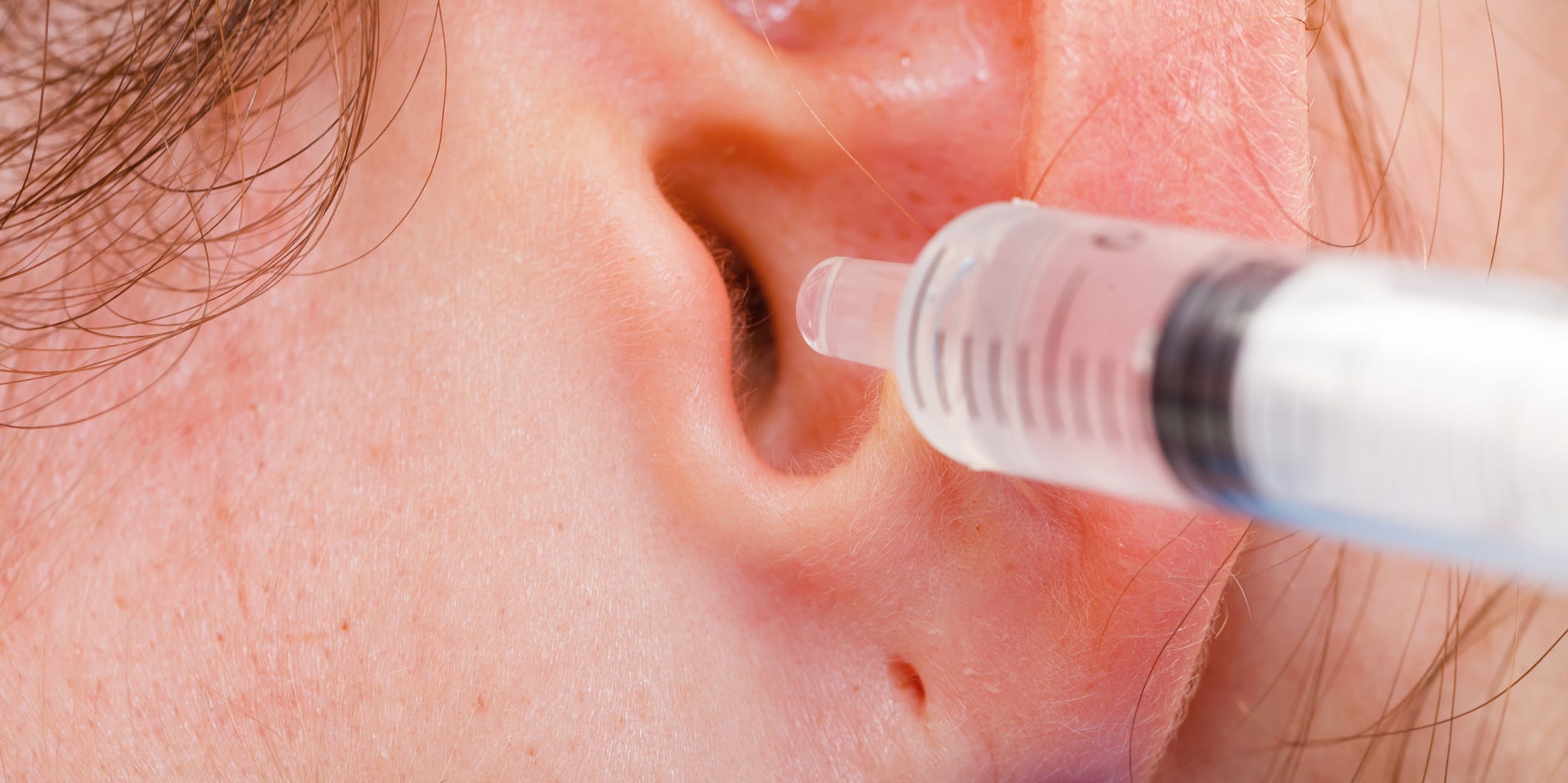 Person with a liquid syringe near their ear.