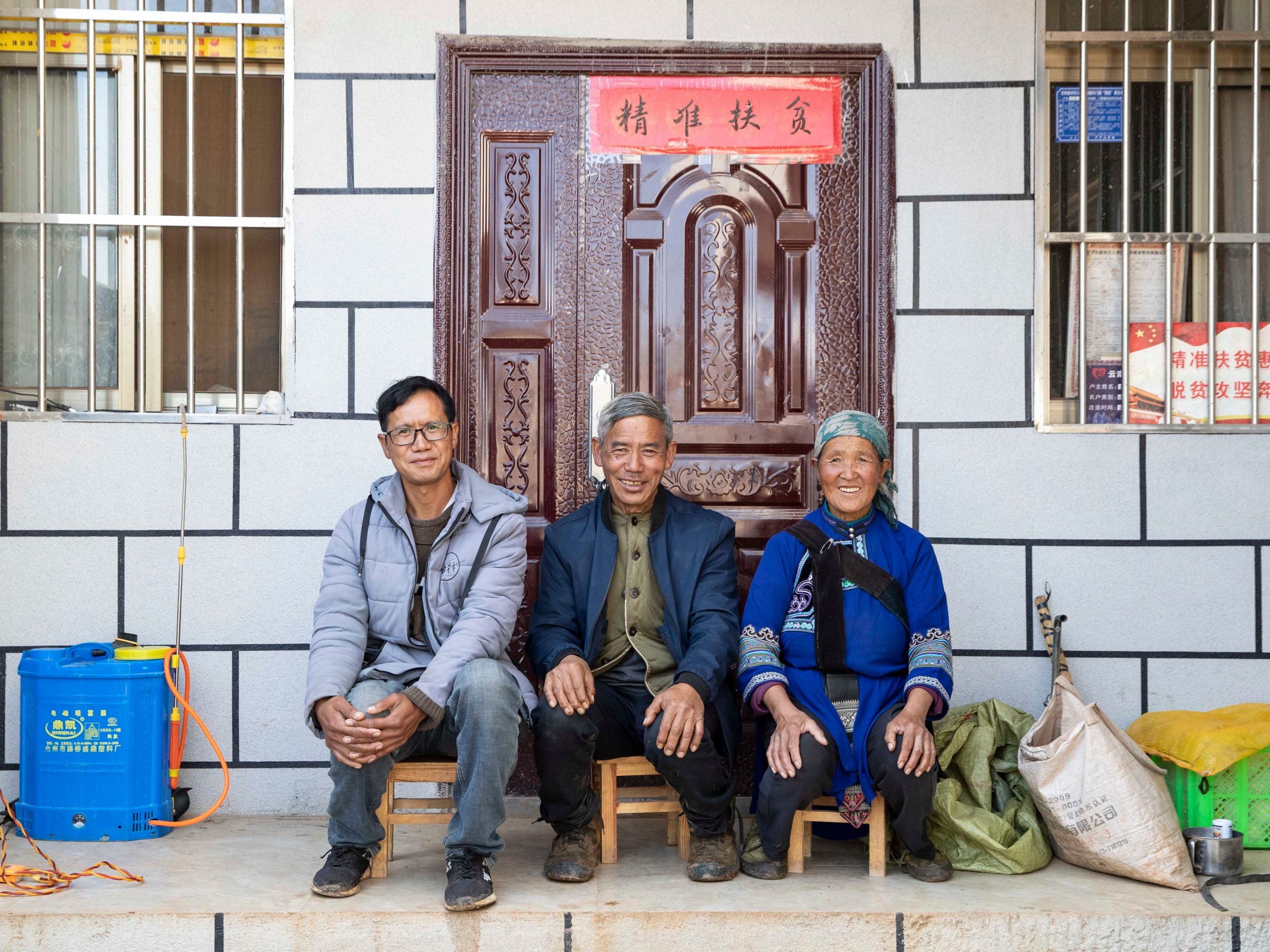 A young man sitting in front of his house in rural China with his parents