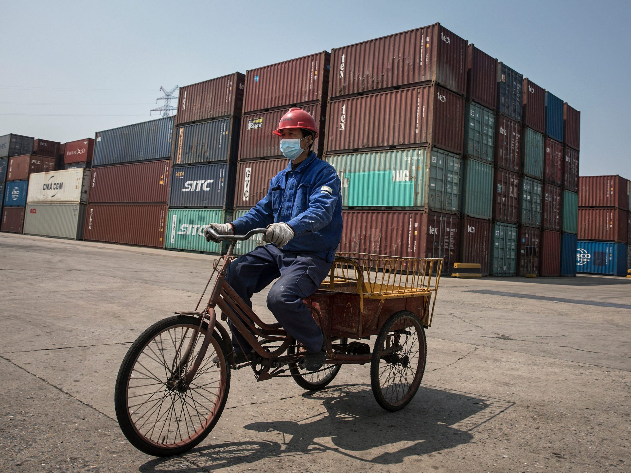 A man on a bicycle in front of containers at a port in China.