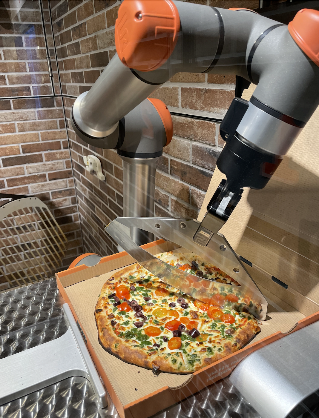 A robotic arm slices a pizza in a cardboard box