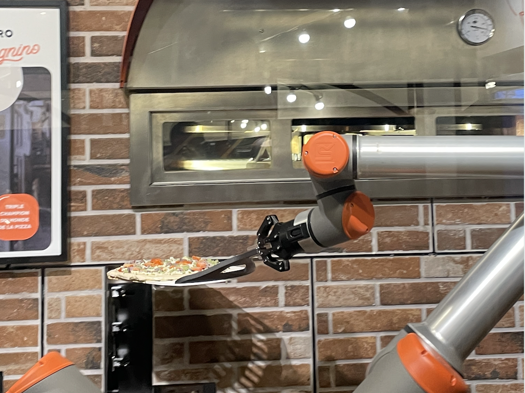 Robotic arm holding pizza moves it into the oven