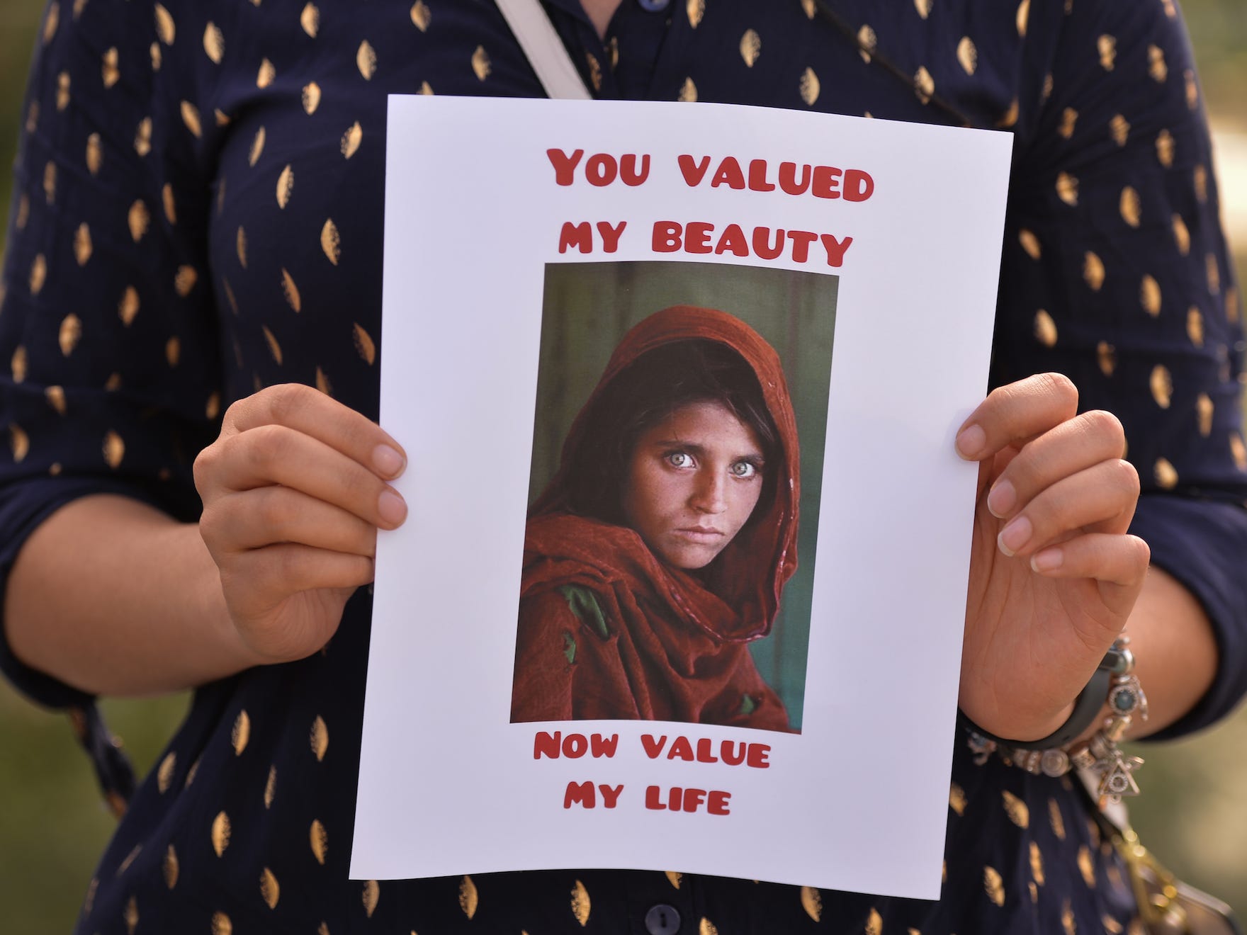 a protester holding up a sign with the photo of the afghan girl on it, which reads 'You Valued My Beauty, Now You Value My Life.'