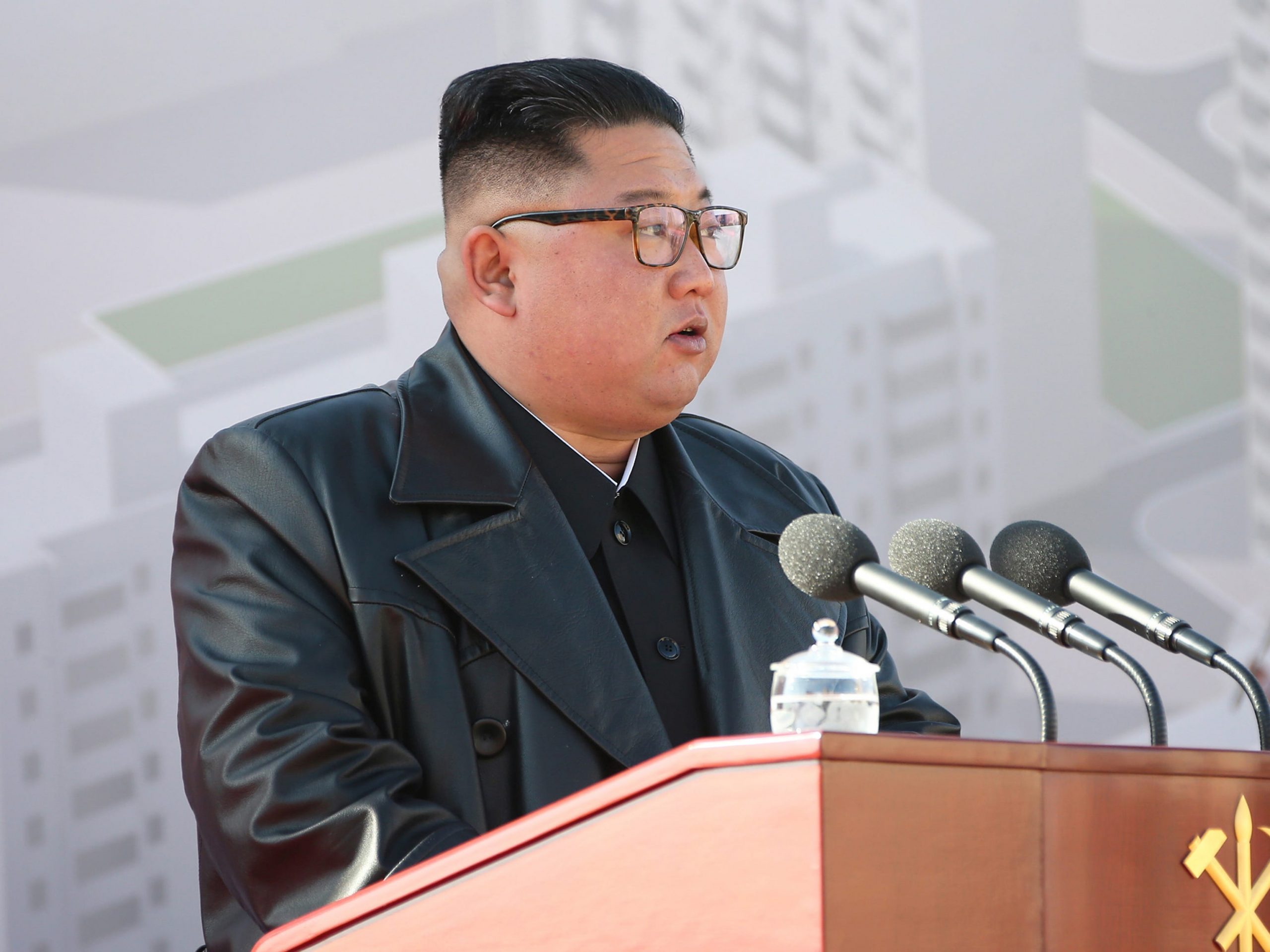 Kim Jong Un standing at a lectern, wearing a leather jacket.