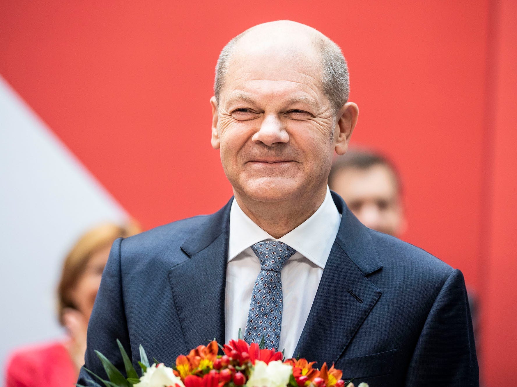 Olaf Scholz, wearing a suit and carrying a bouquet of flowers smiles after his party, the SPD, gathered the most votes in Germany's preliminary elections  results