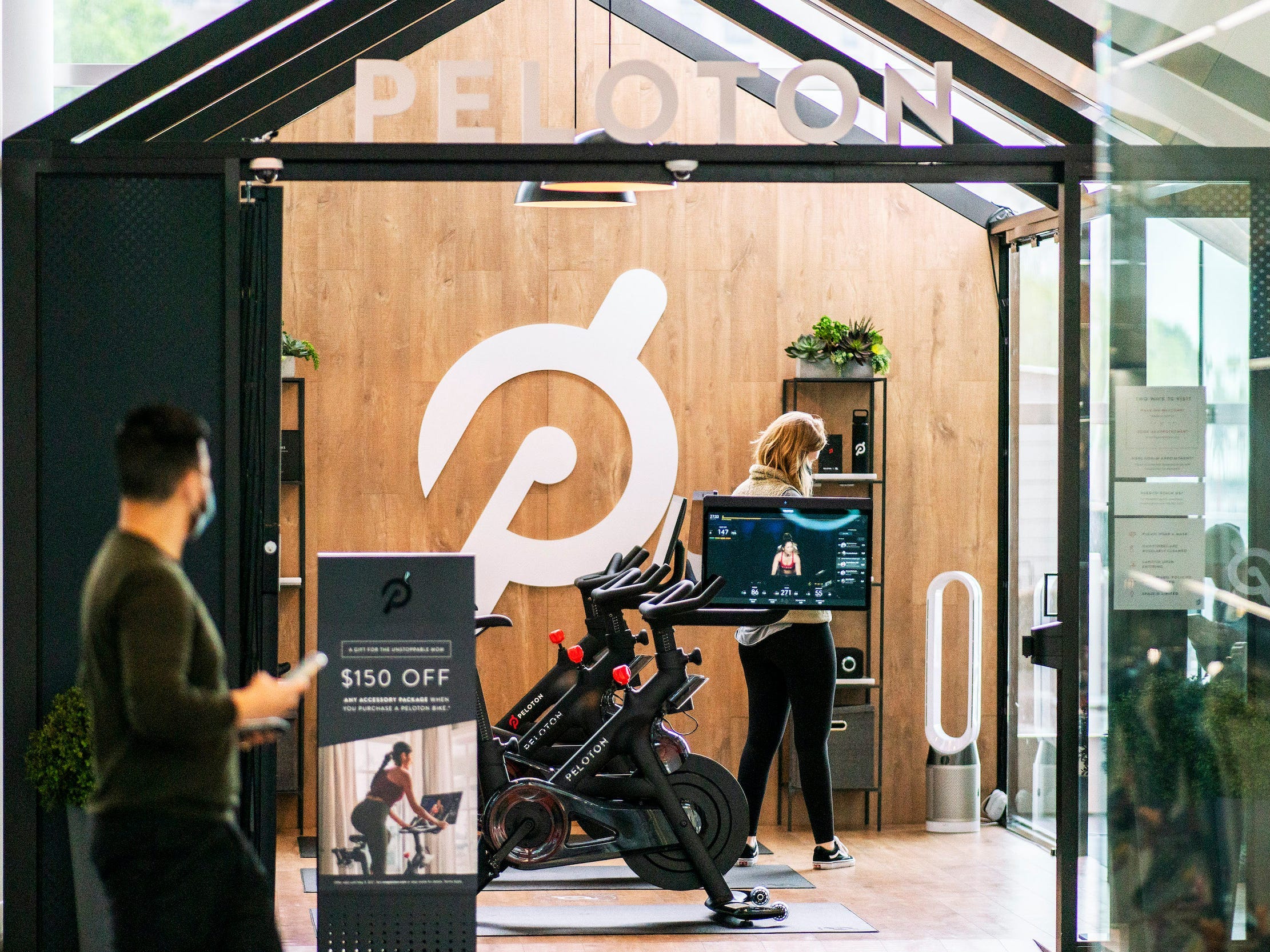 Man walks by Peloton store will bikes and woman in workout gear standing inside