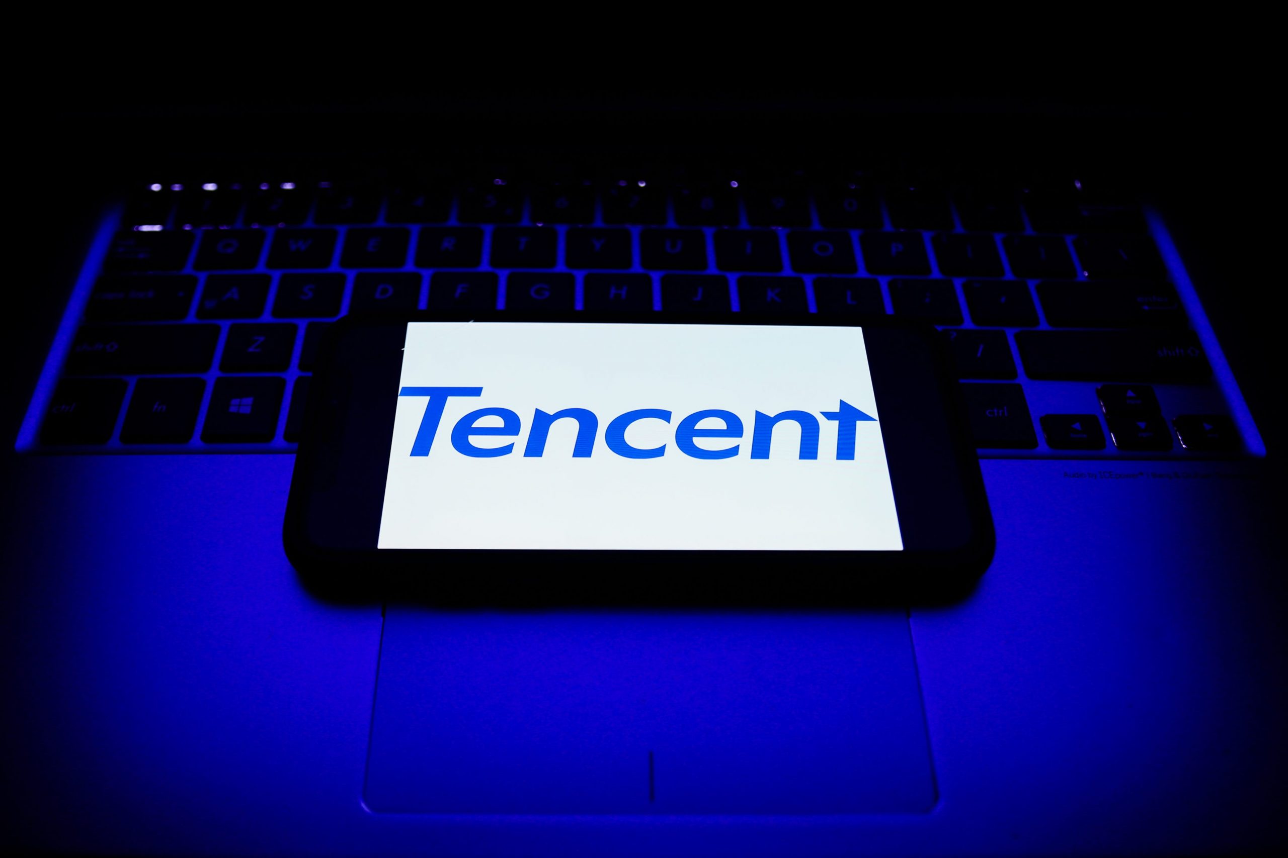 A phone displays Tencent's logo on top of a laptop keyboard