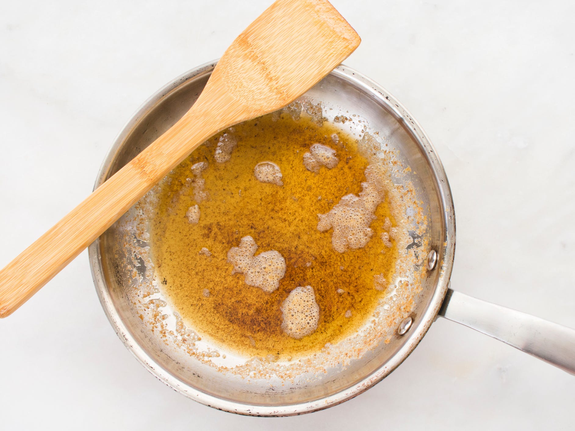 A top-down view of brown butter in a skillet with a wooden spatula resting on the pan