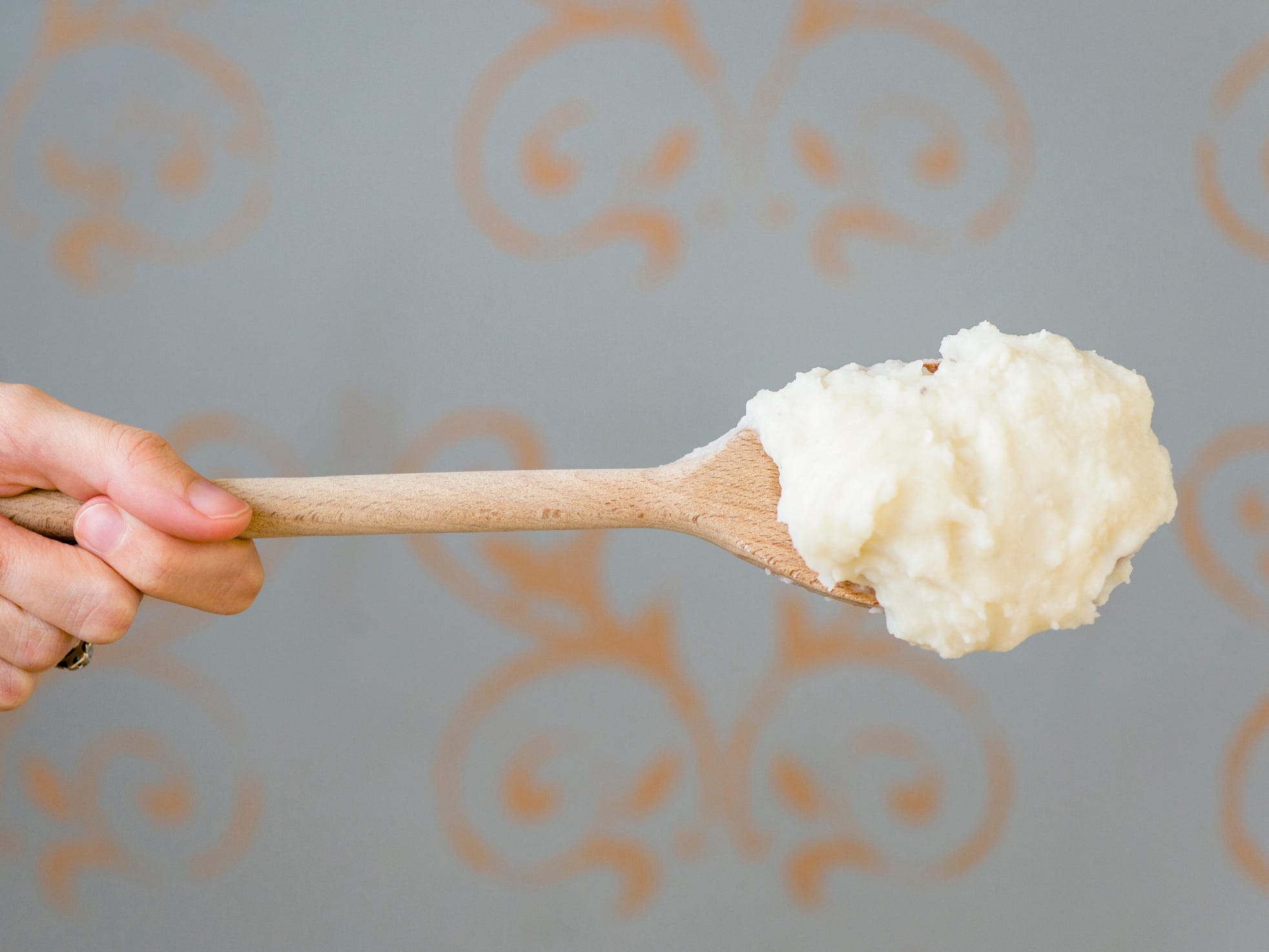 A wooden spoonful of mashed potatoes help perpendicularly to the camera