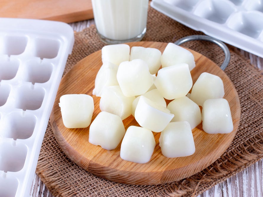 Milk ice cubes on a cutting board a white wooden table.