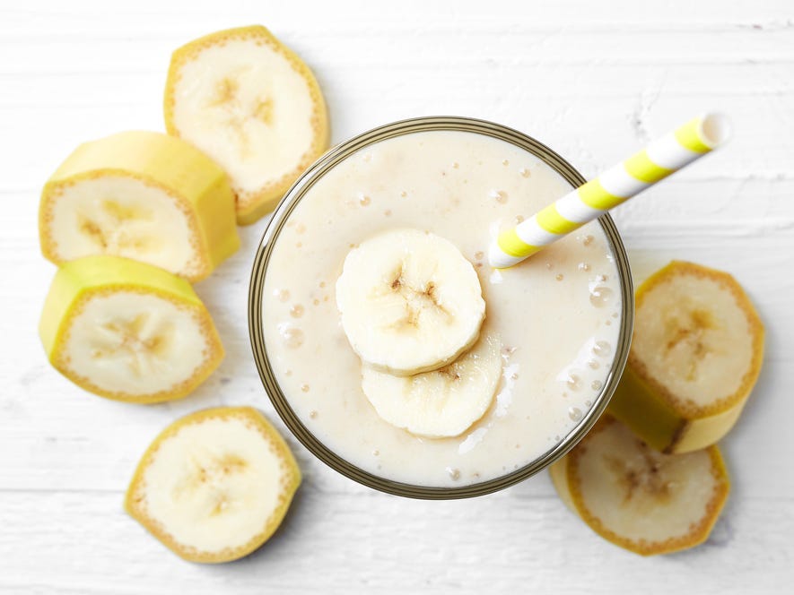 Glass of banana smoothie on white wooden background from top view.