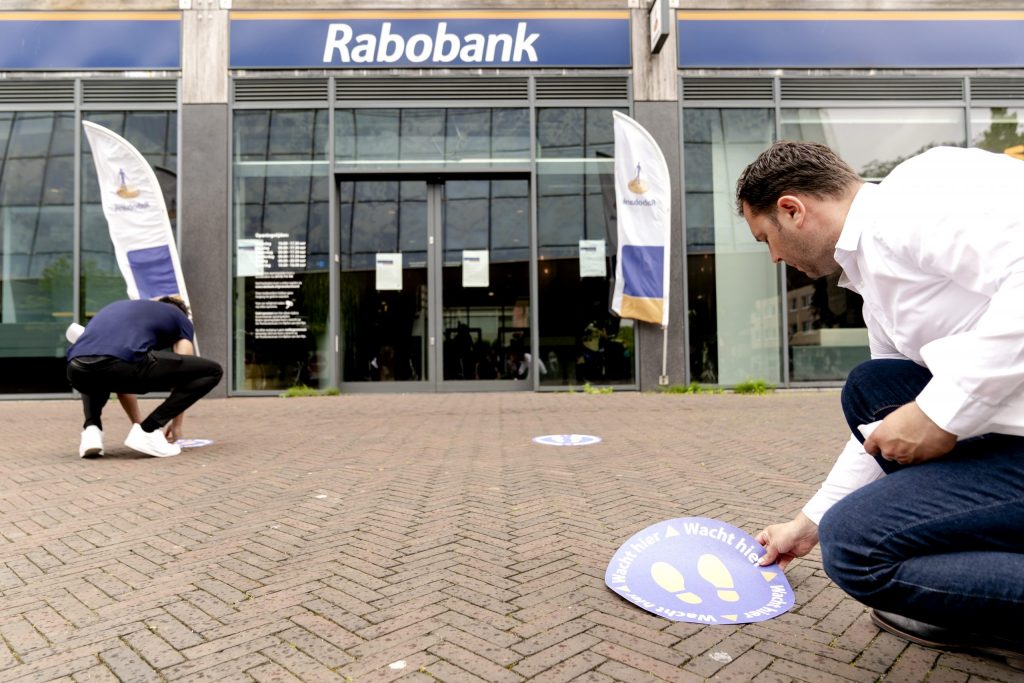 Medewerkers van de Rabobank brengen stickers aan voor het houden van 1,5 meter afstand bij een filiaal in Alphen aan de Rijn.