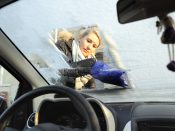 Een vrouw krabt de ruiten van een auto.