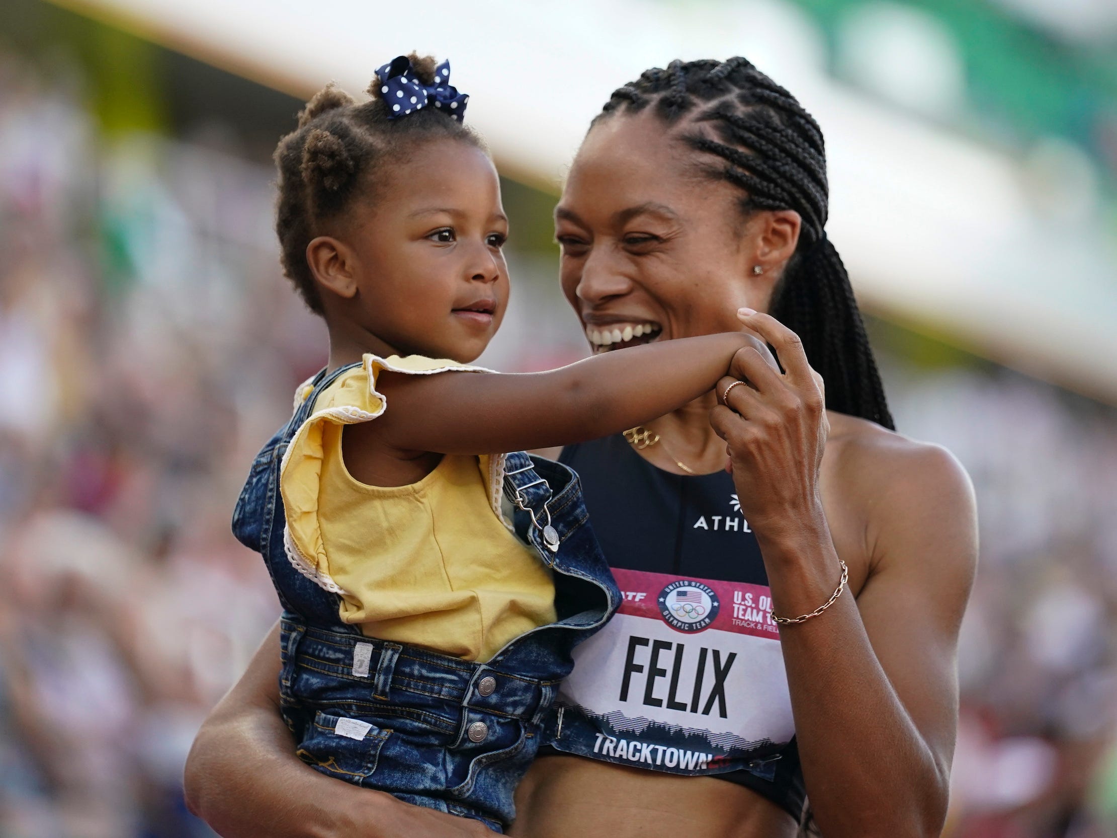 Allyson Felix smiles while holding her daughter in her arms with crowds in the background