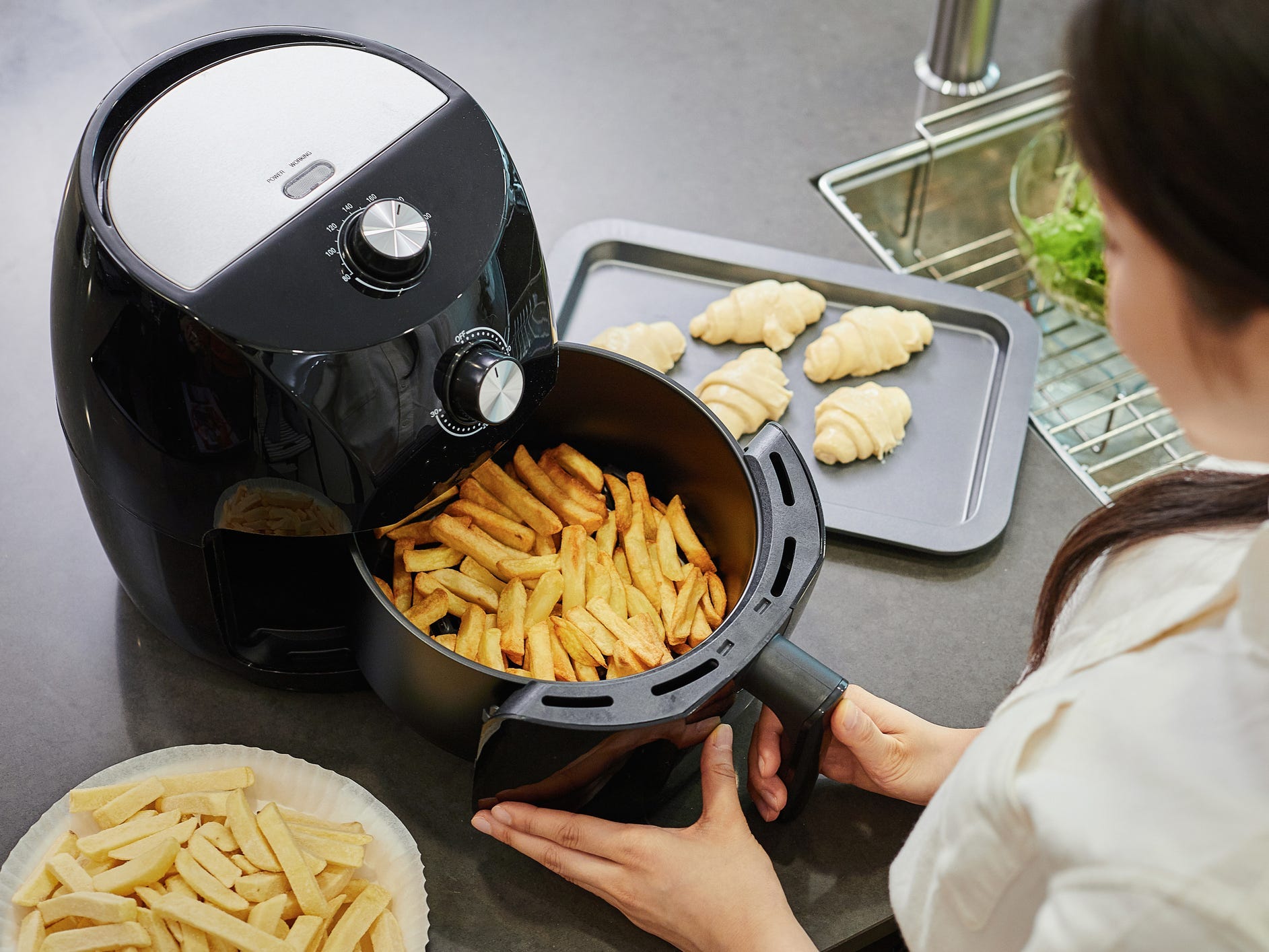 A person starting a batch of french fries in an air fryer