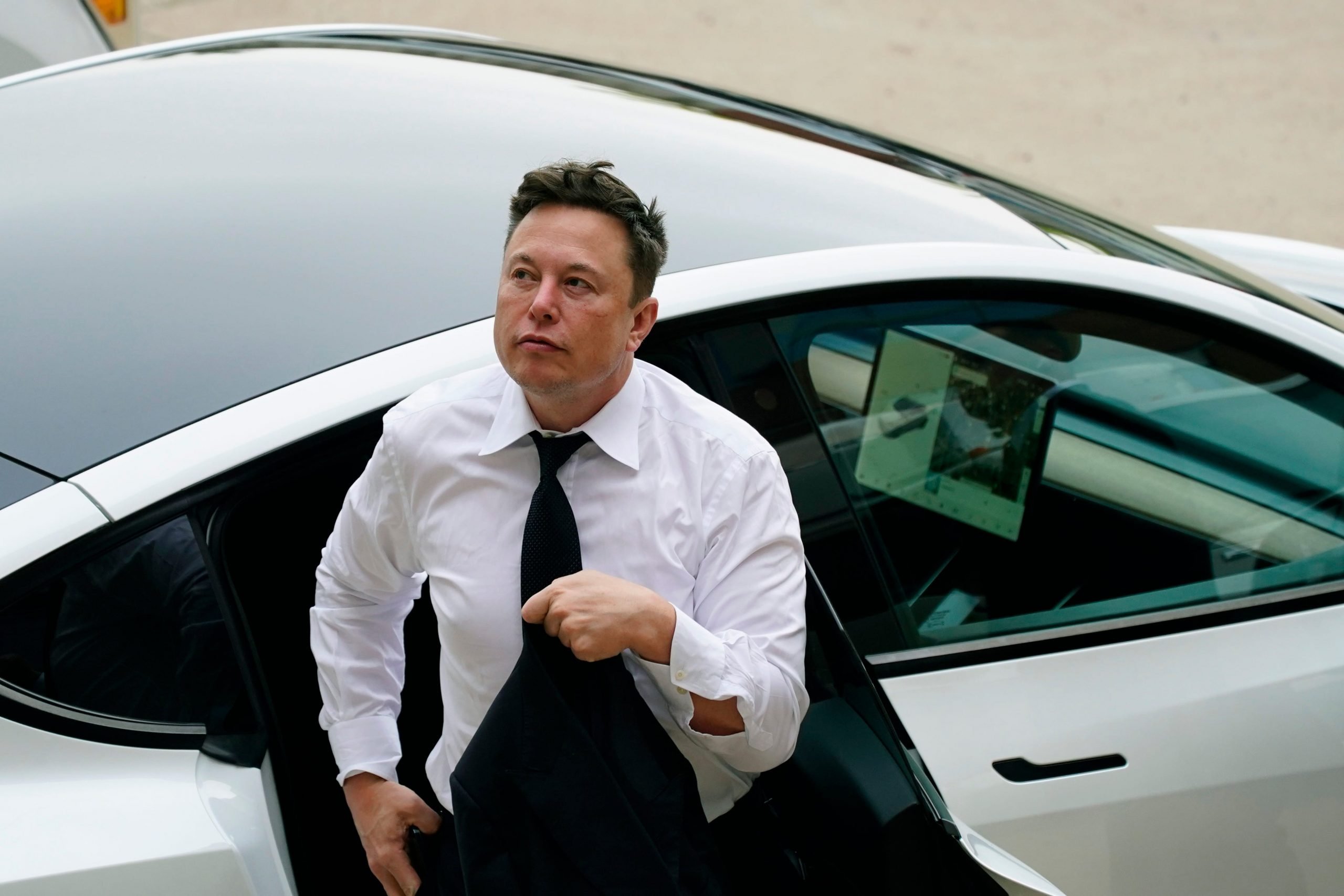 Tesla CEO Elon Musk in a white shirt and tie exits the backseat of a white Tesla