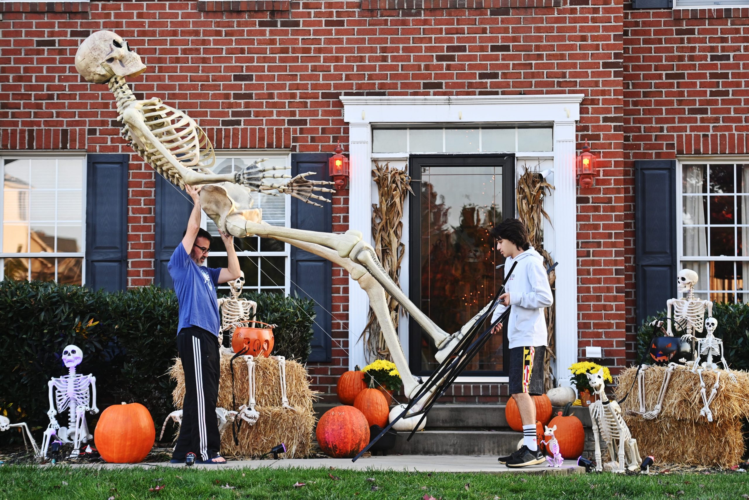 A father and son carry their 12-foot-tall Home Depot skeleton into storage after Halloween.